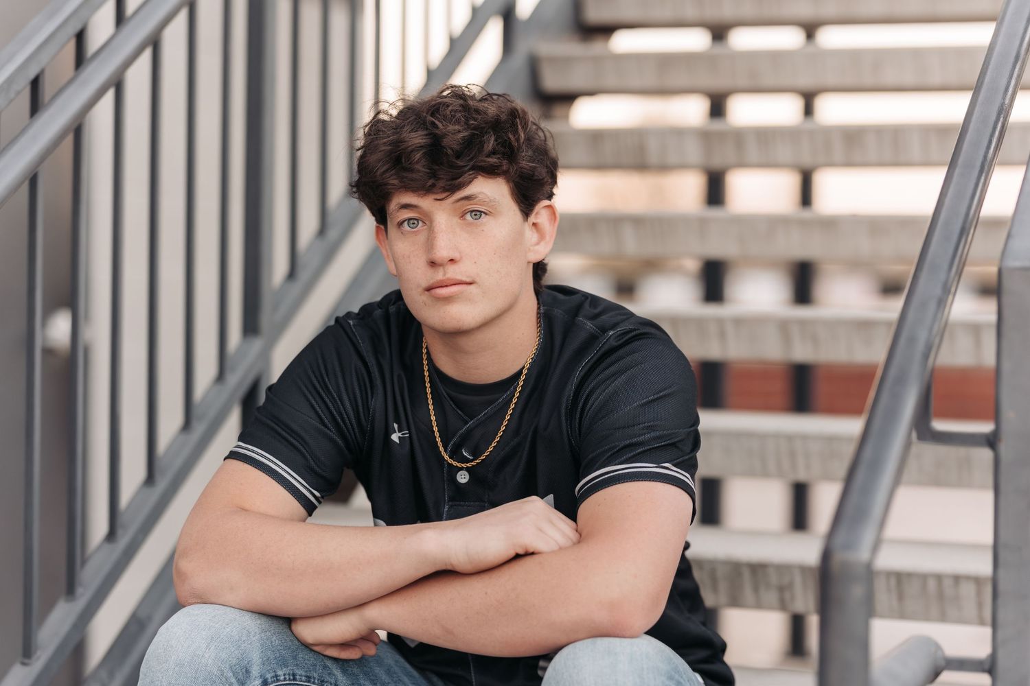 Young athlete sitting casually on concrete stairs wearing a dark t-shirt and necklace.