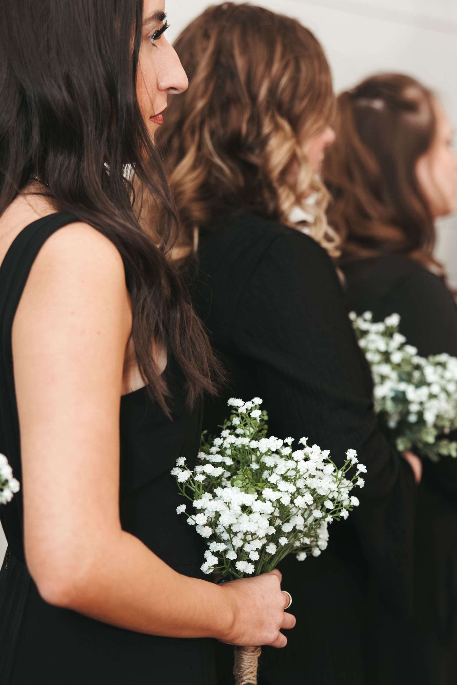 Bridesmaids in black dresses hold delicate white baby's breath bouquets during the ceremony.