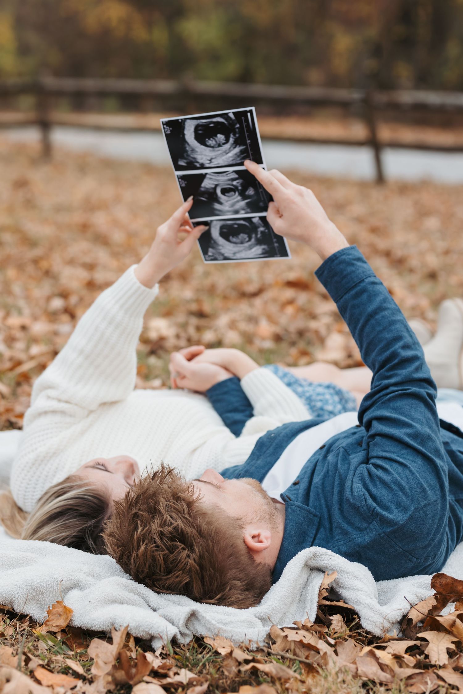 Couple lying in autumn leaves viewing ultrasound photos together.