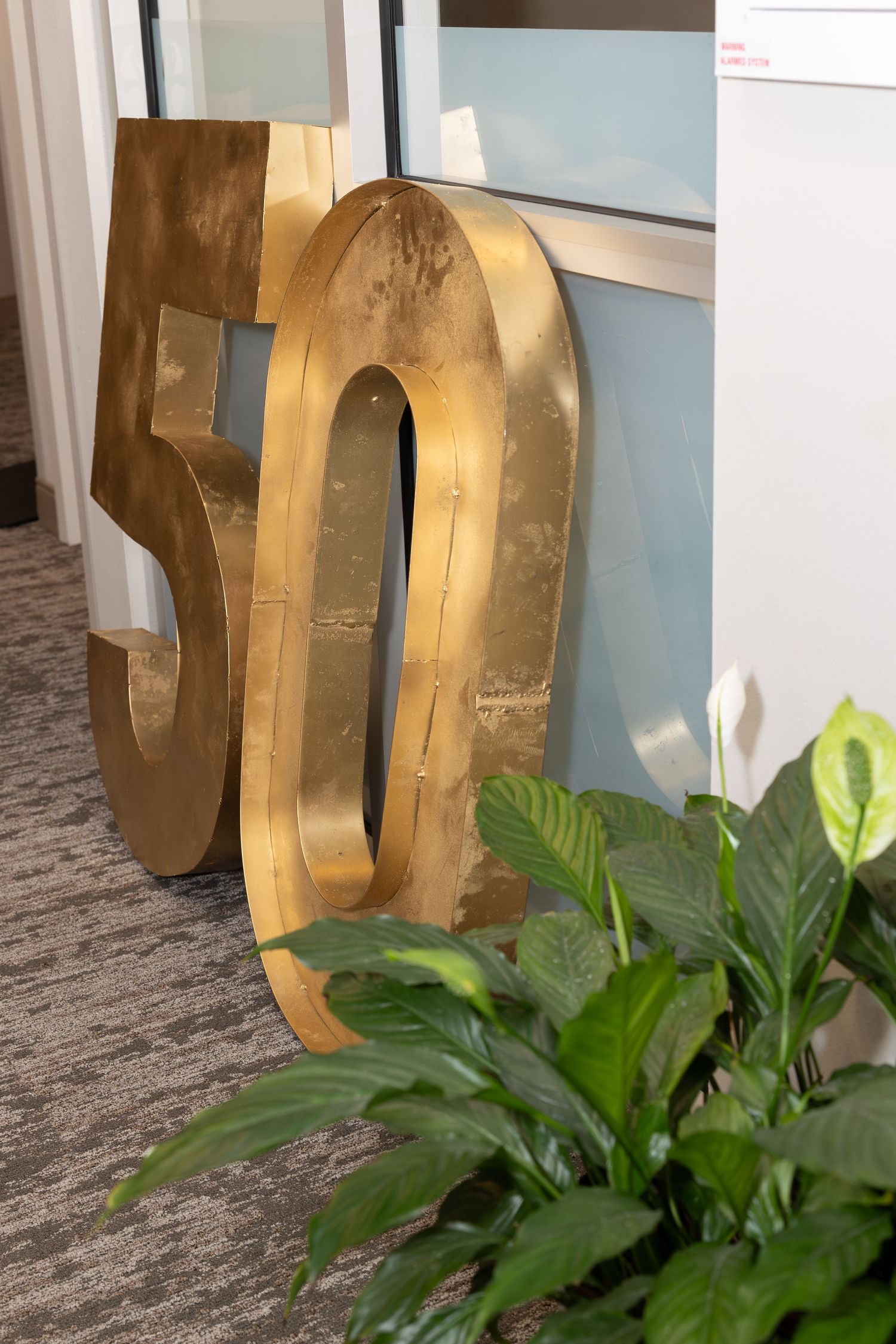 Large golden metallic number 50 display with decorative plant in office setting.