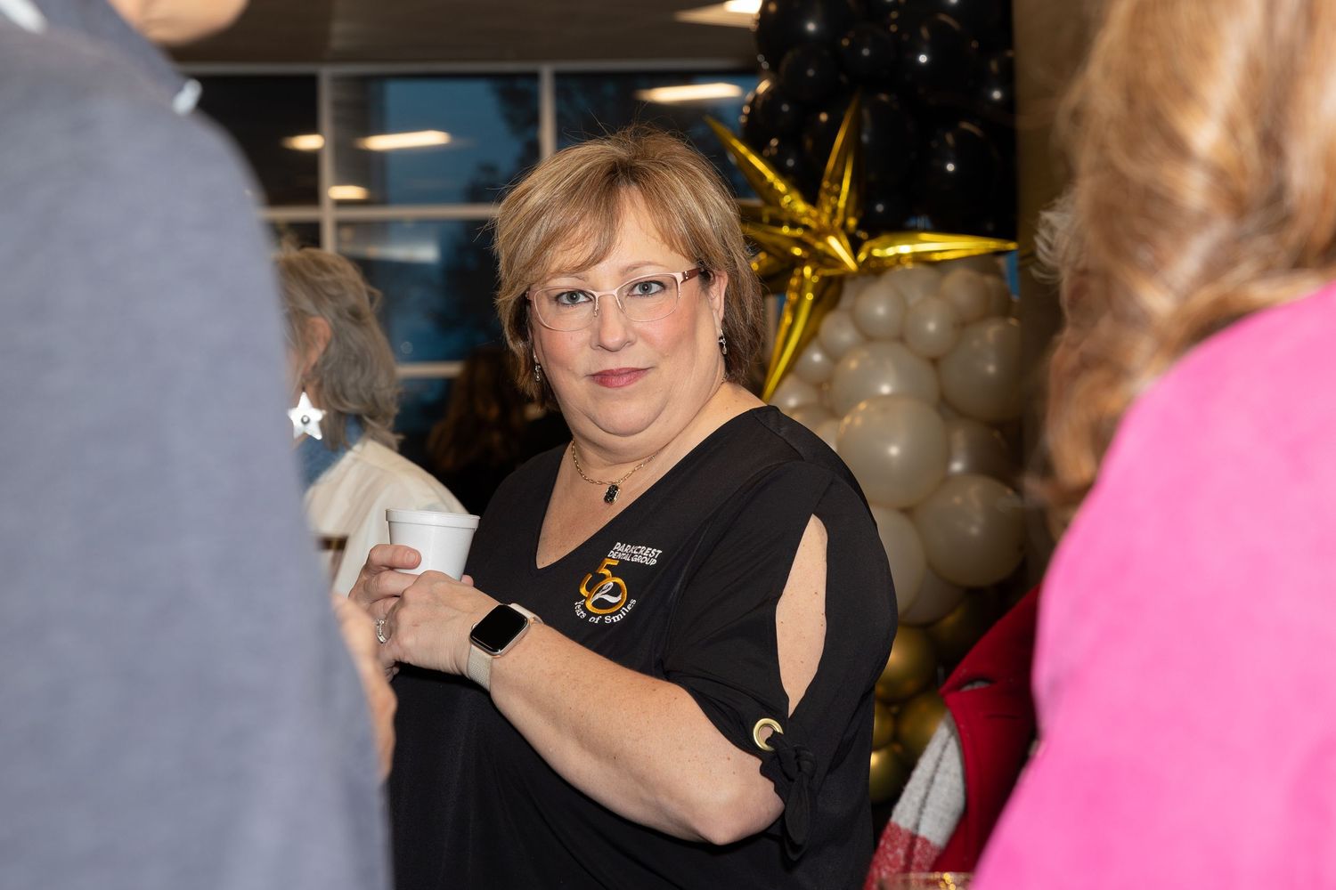 Person wearing black attire with smartwatch mingling at social gathering.