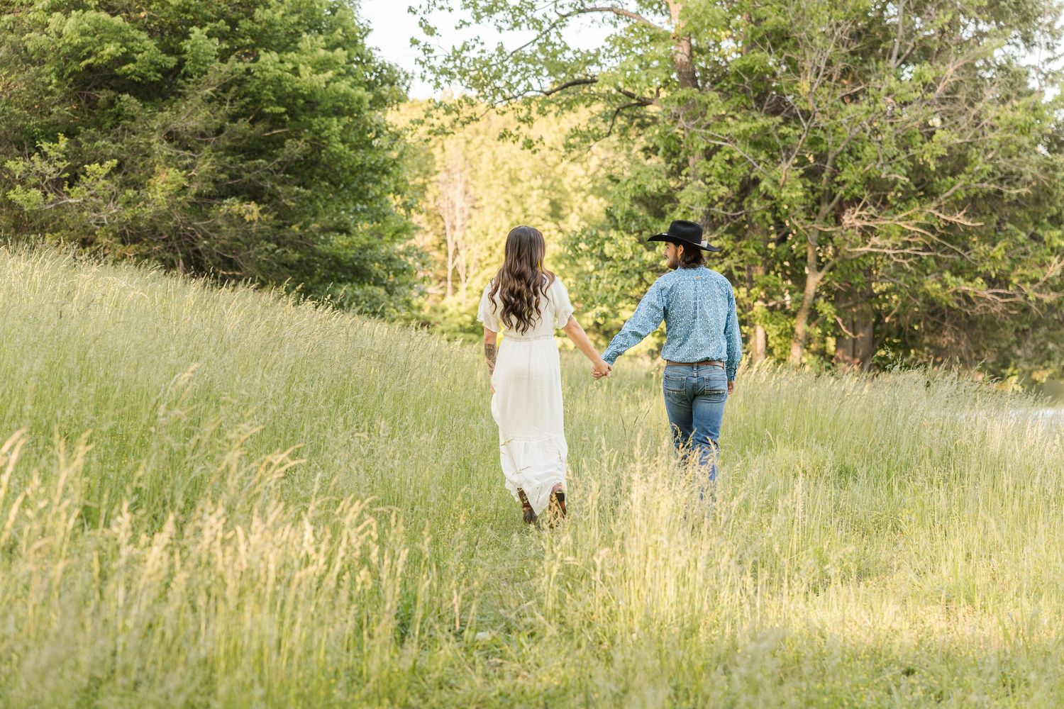 People walking through a sunlit meadow in early fall with tall grass and trees in the background.