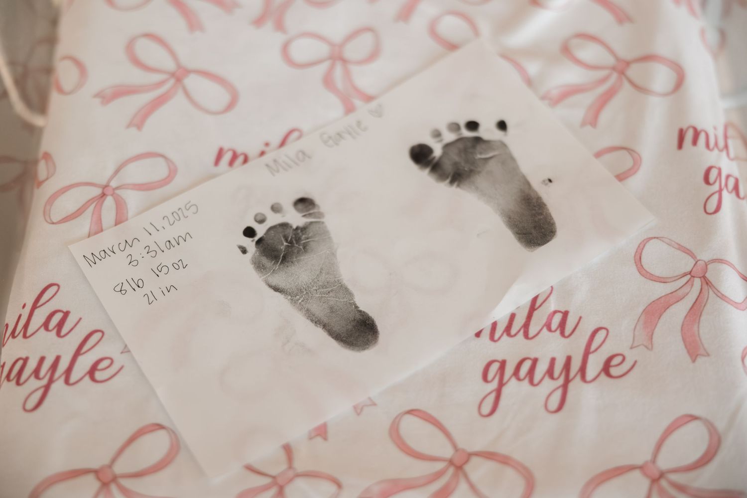 Personalized baby footprint art with pink bow decorations and names written in cursive script on white paper.