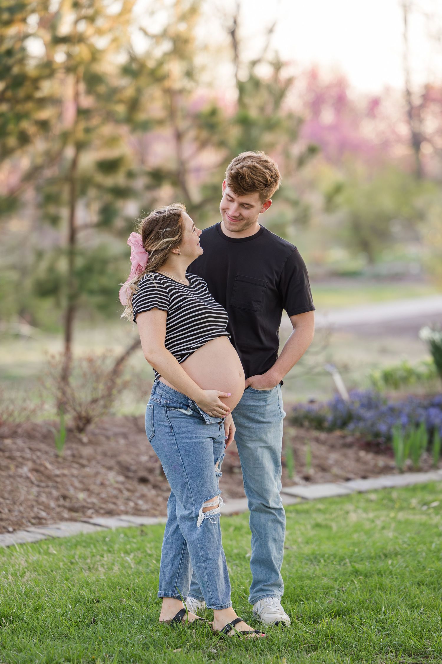 An expecting couple stands together on a garden path during a spring maternity photoshoot.