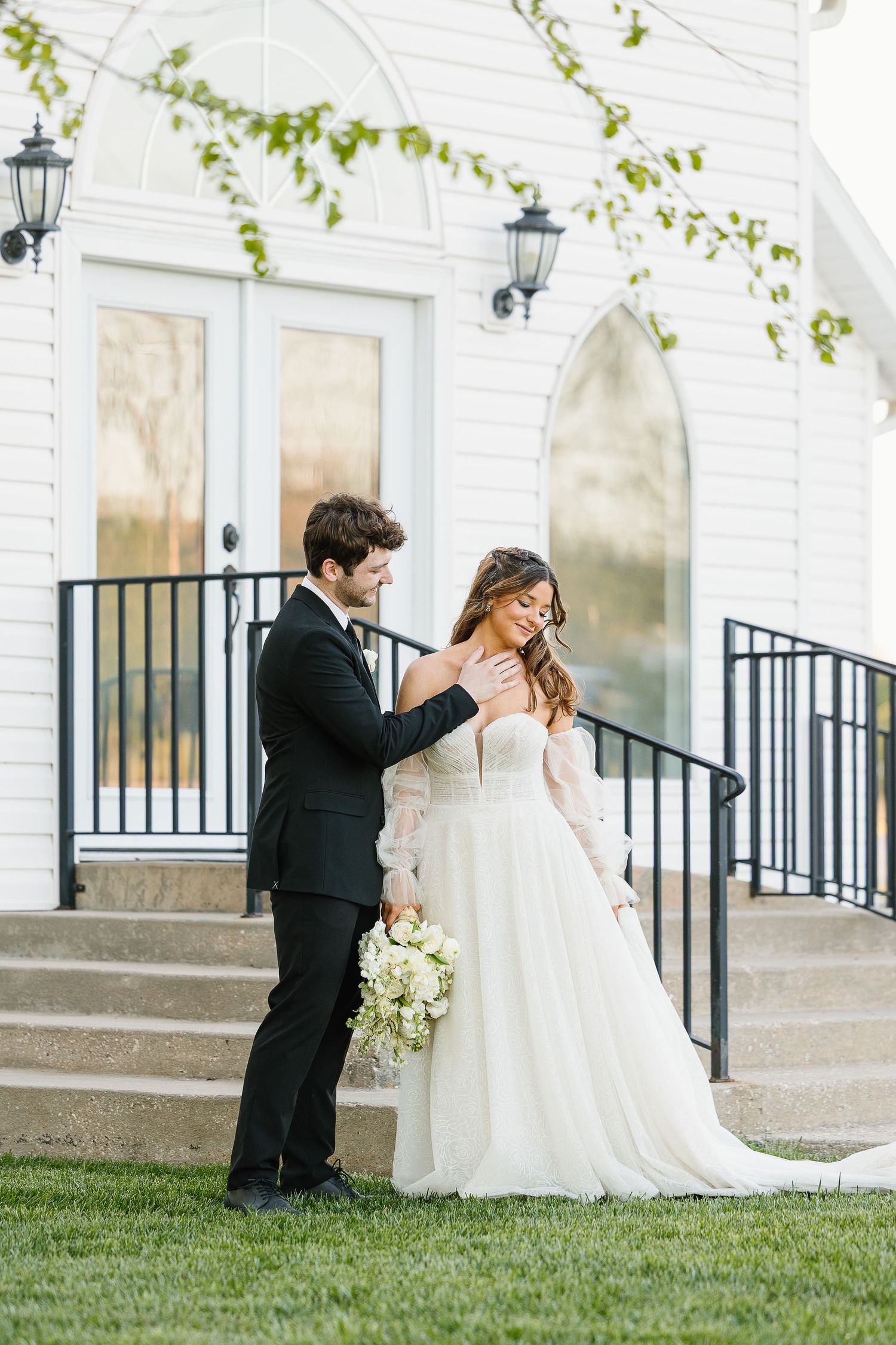 A bride and groom share a romantic kiss in front of a white church building during a wedding photo session.