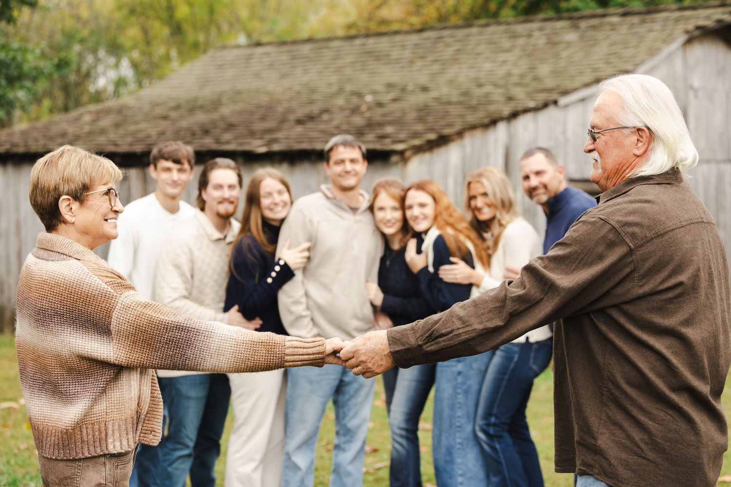 A group of people stand in a line outdoors playing a team-building game by holding hands in front of a rustic building.