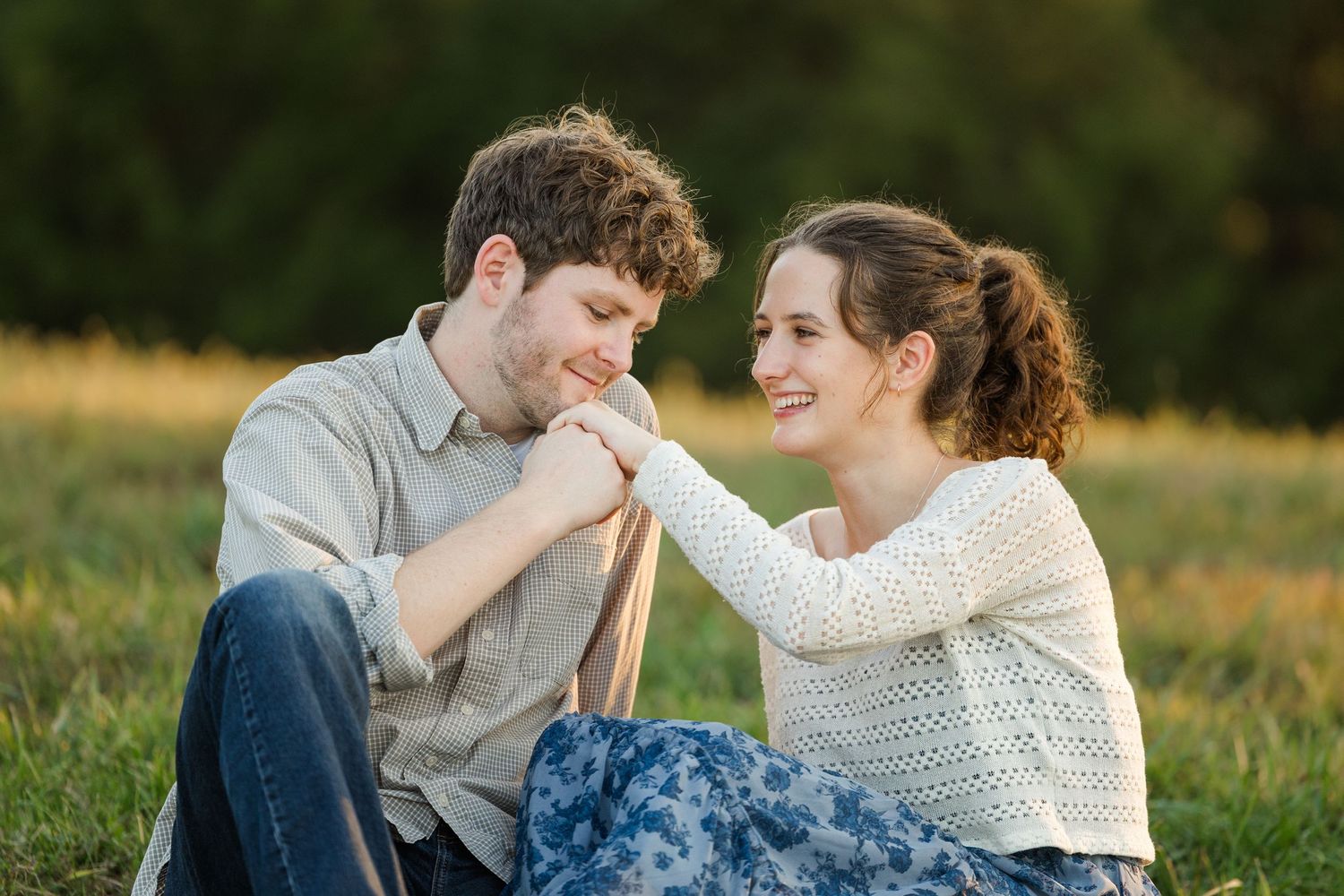 A couple sits together in a grassy field during golden hour, sharing intimate moments in casual attire.
