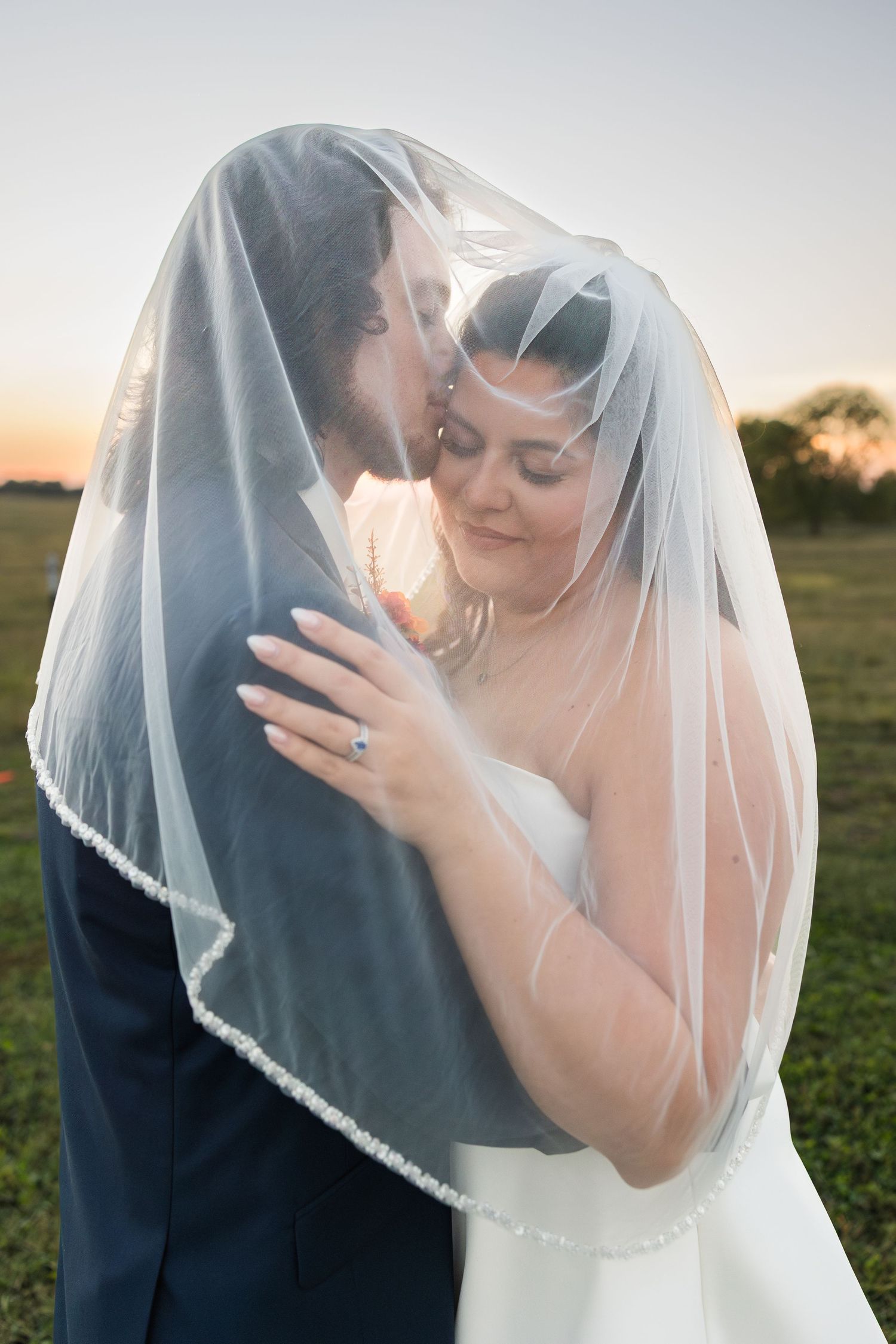 Tender wedding portrait under a delicate white veil against soft natural lighting.