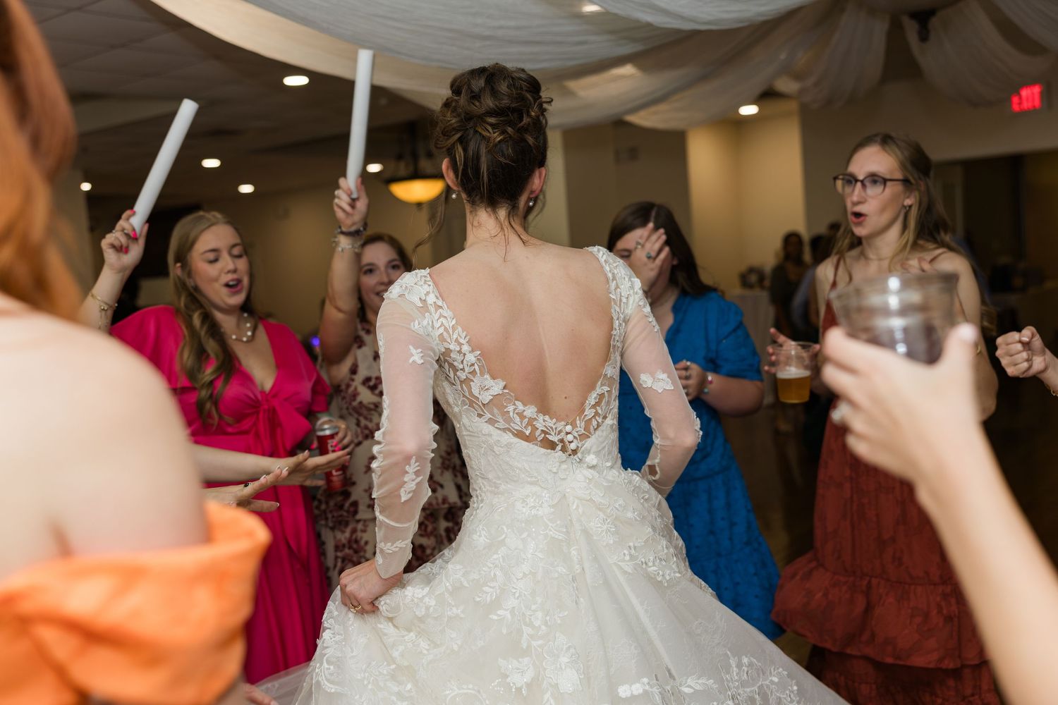 Bride in backless lace gown dances surrounded by colorful bridesmaids at lively wedding reception.