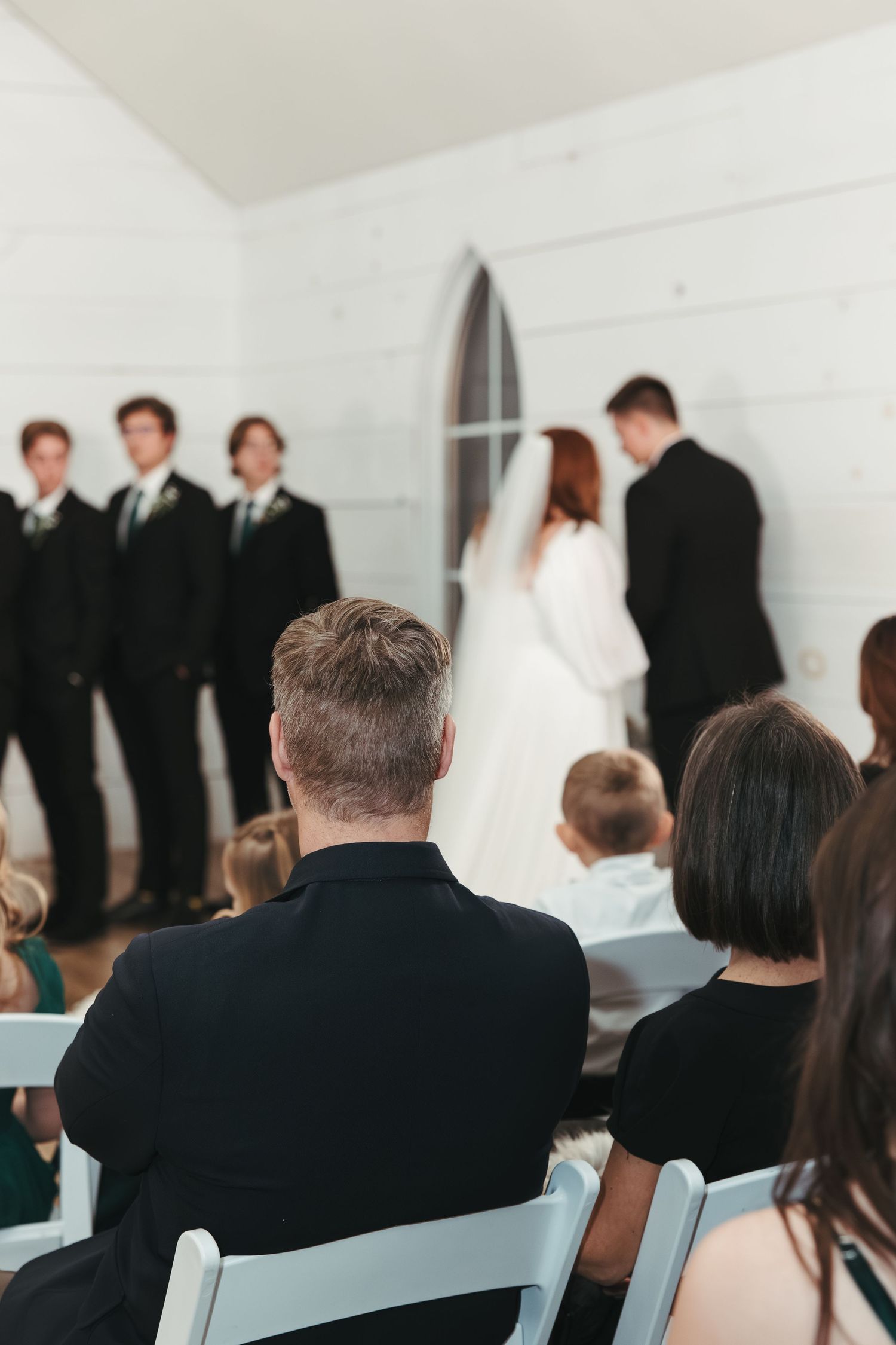 A wedding ceremony in progress viewed from behind guests in white folding chairs.