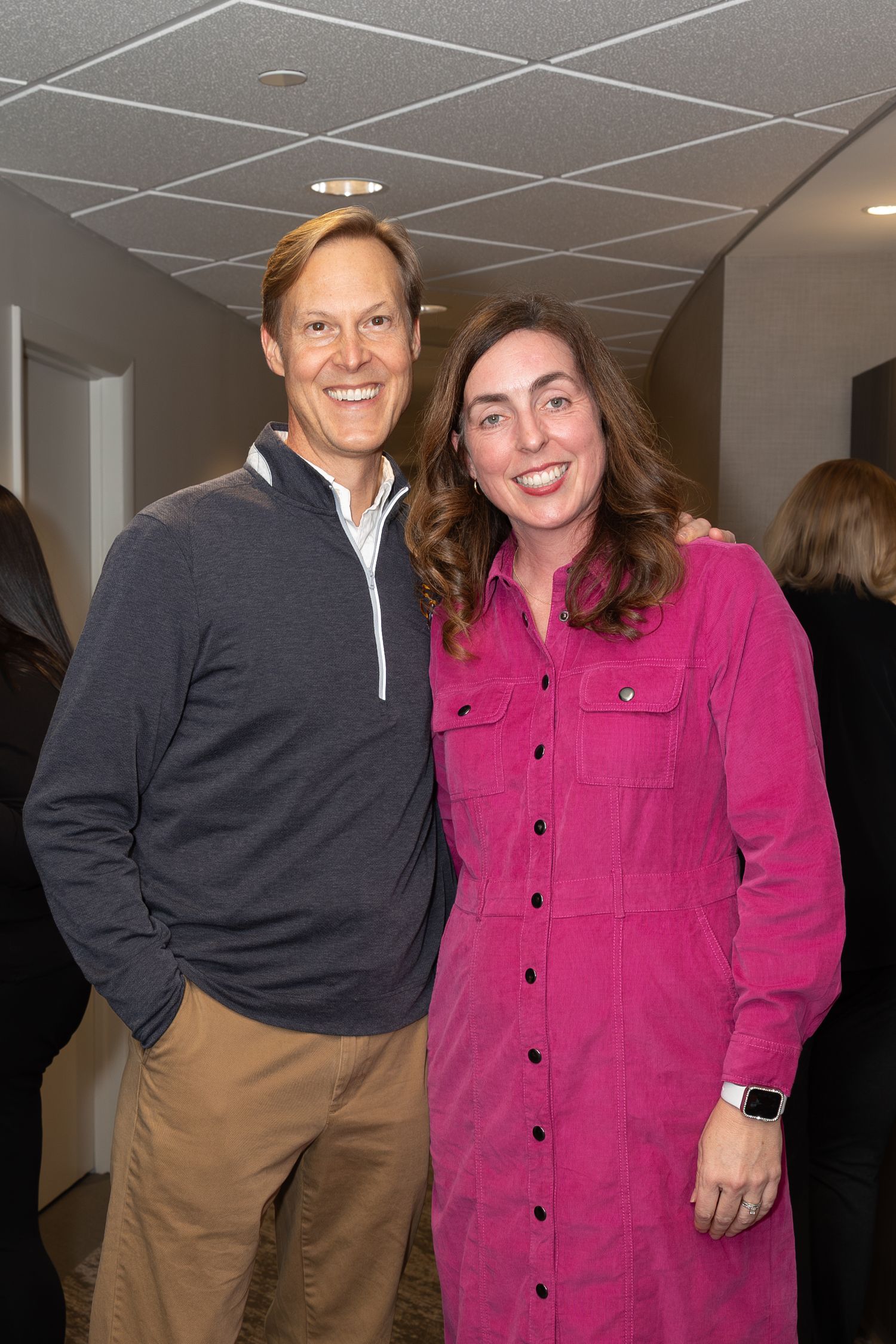 Two attendees at an office event, one wearing a pink dress and one in a gray pullover.