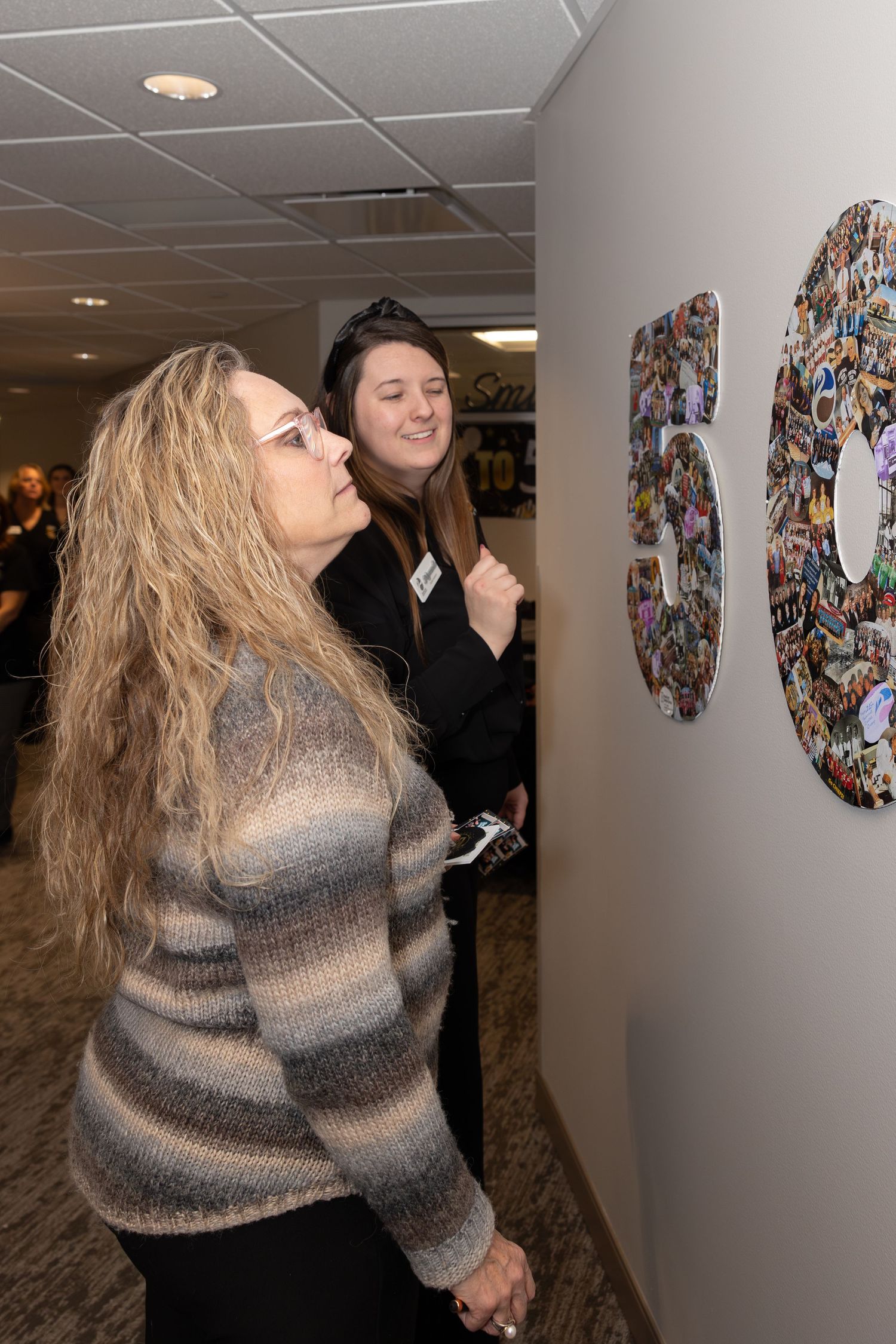 Two people examining decorative wall art in an office corridor.
