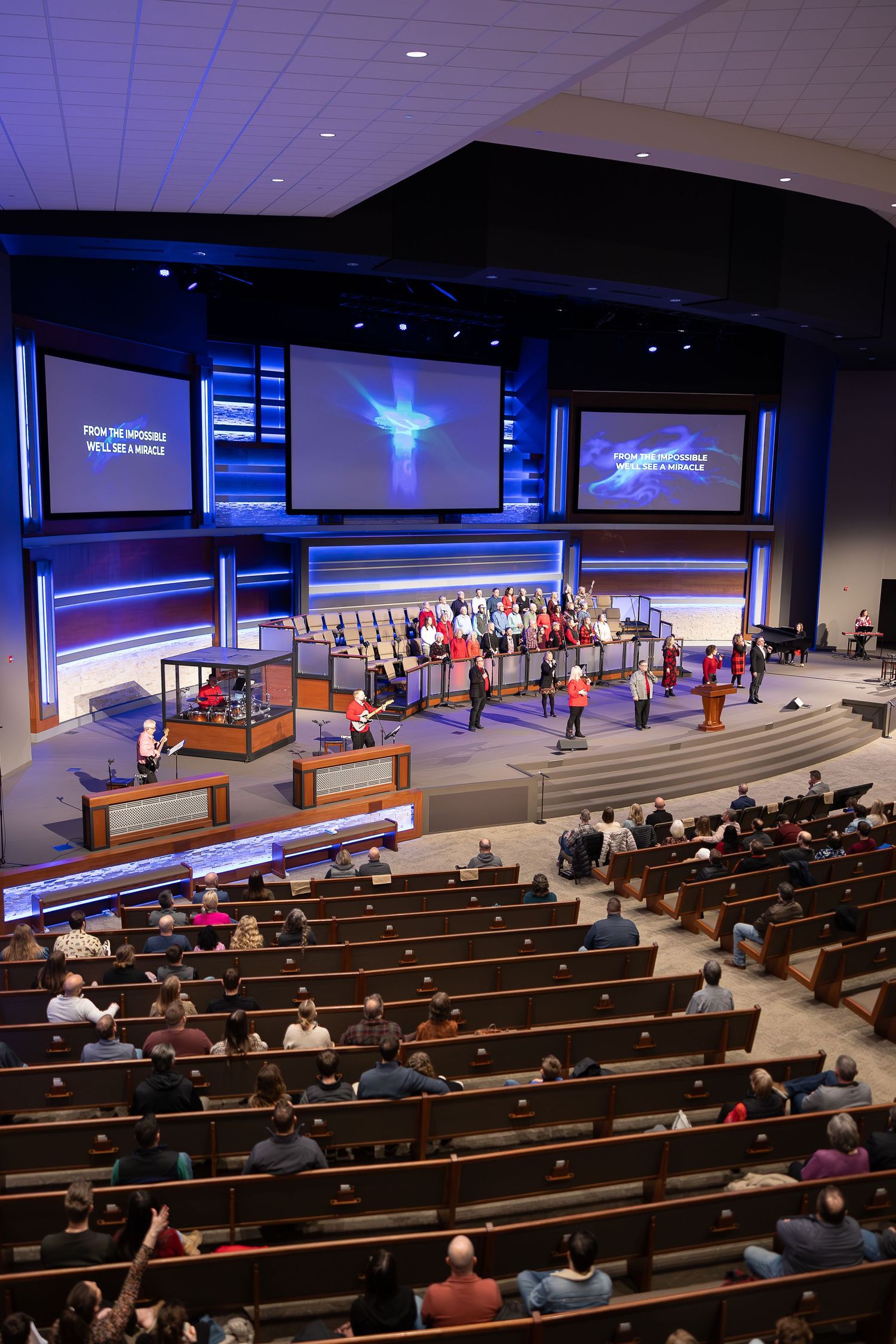 Large modern church sanctuary with multiple video screens and choir performing on stage.