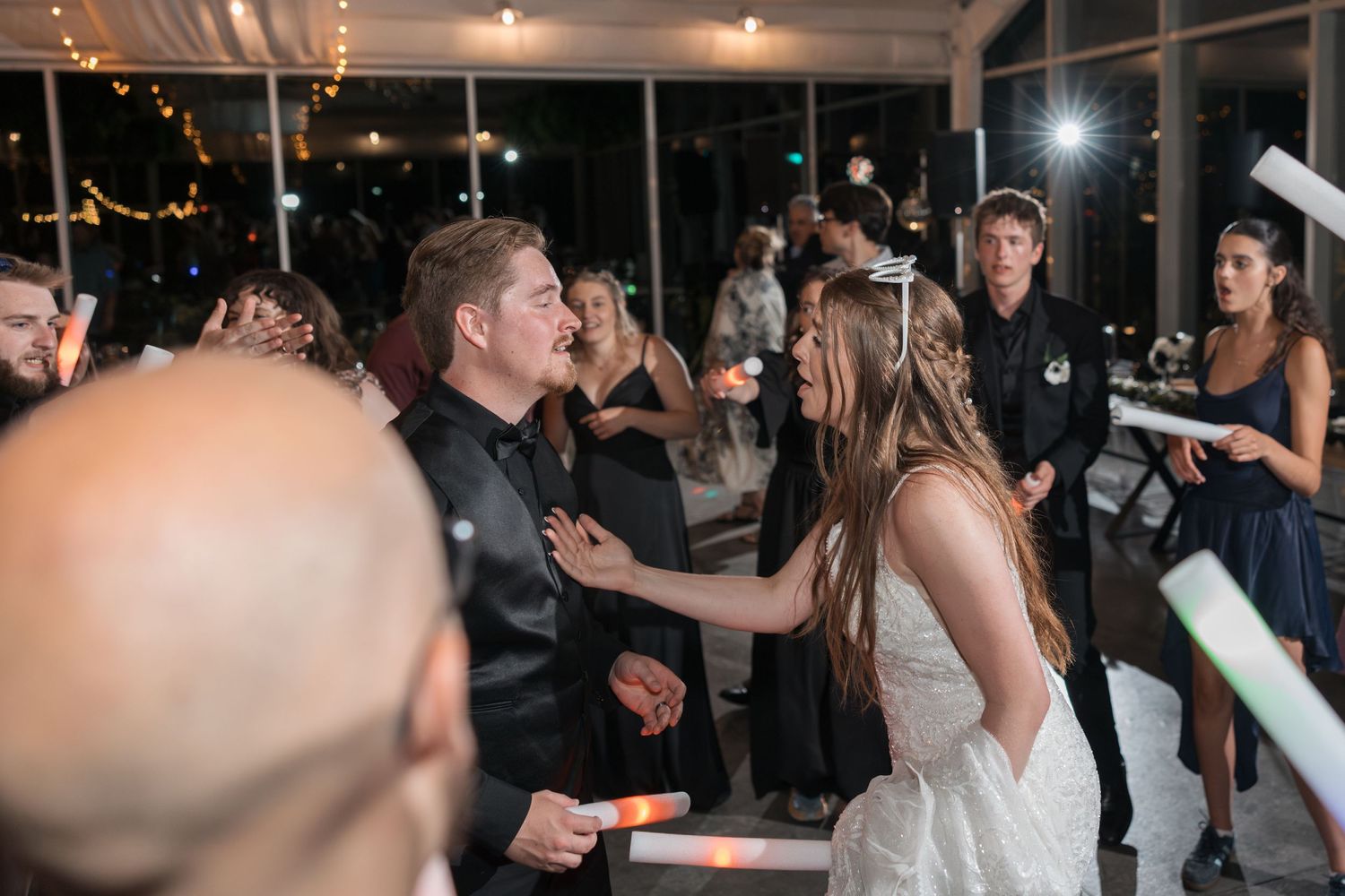 Indoor wedding reception features dancing guests with illuminated party favors.