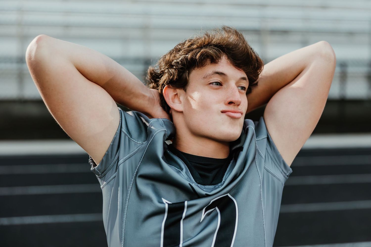 Young athlete in grey shirt relaxes with hands behind head.