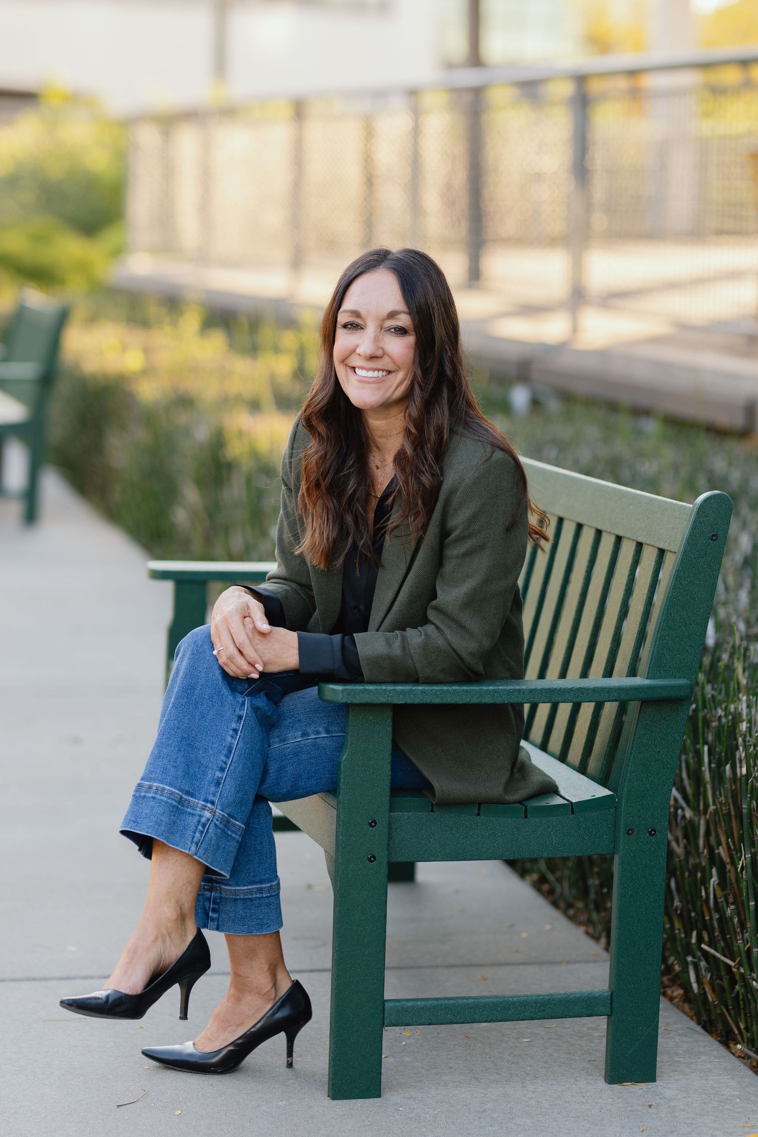 Professional seated on green bench wearing olive blazer and heels in business casual style.
