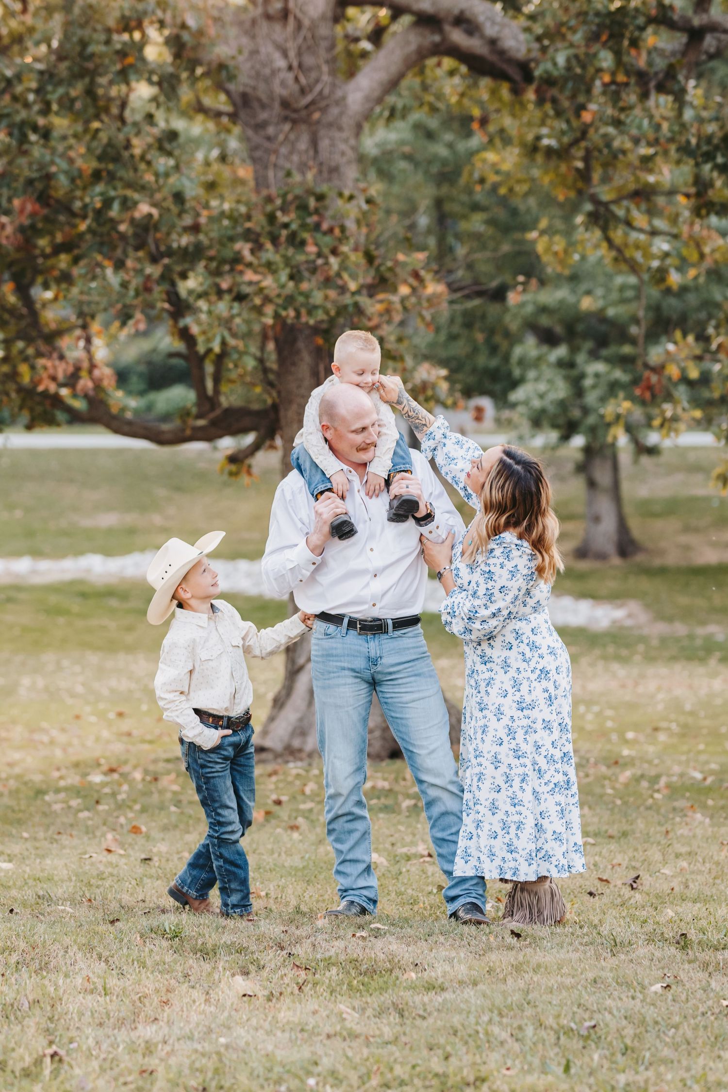 Family wearing casual western attire plays together in a grassy field with autumn trees.