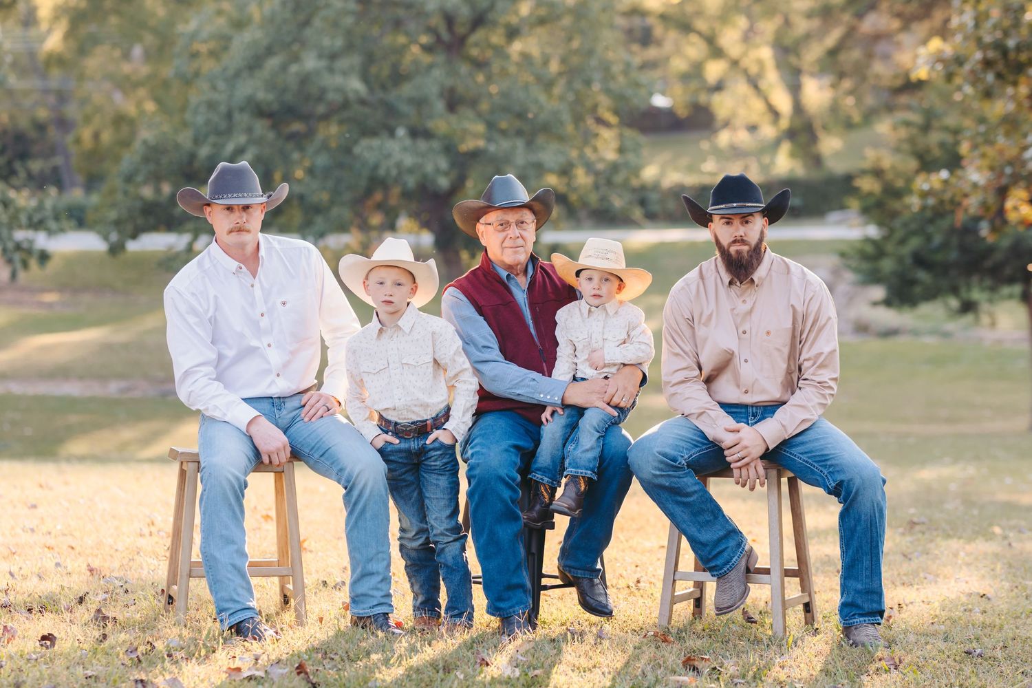 Group in western wear sitting on wooden fence in sunny outdoor setting.