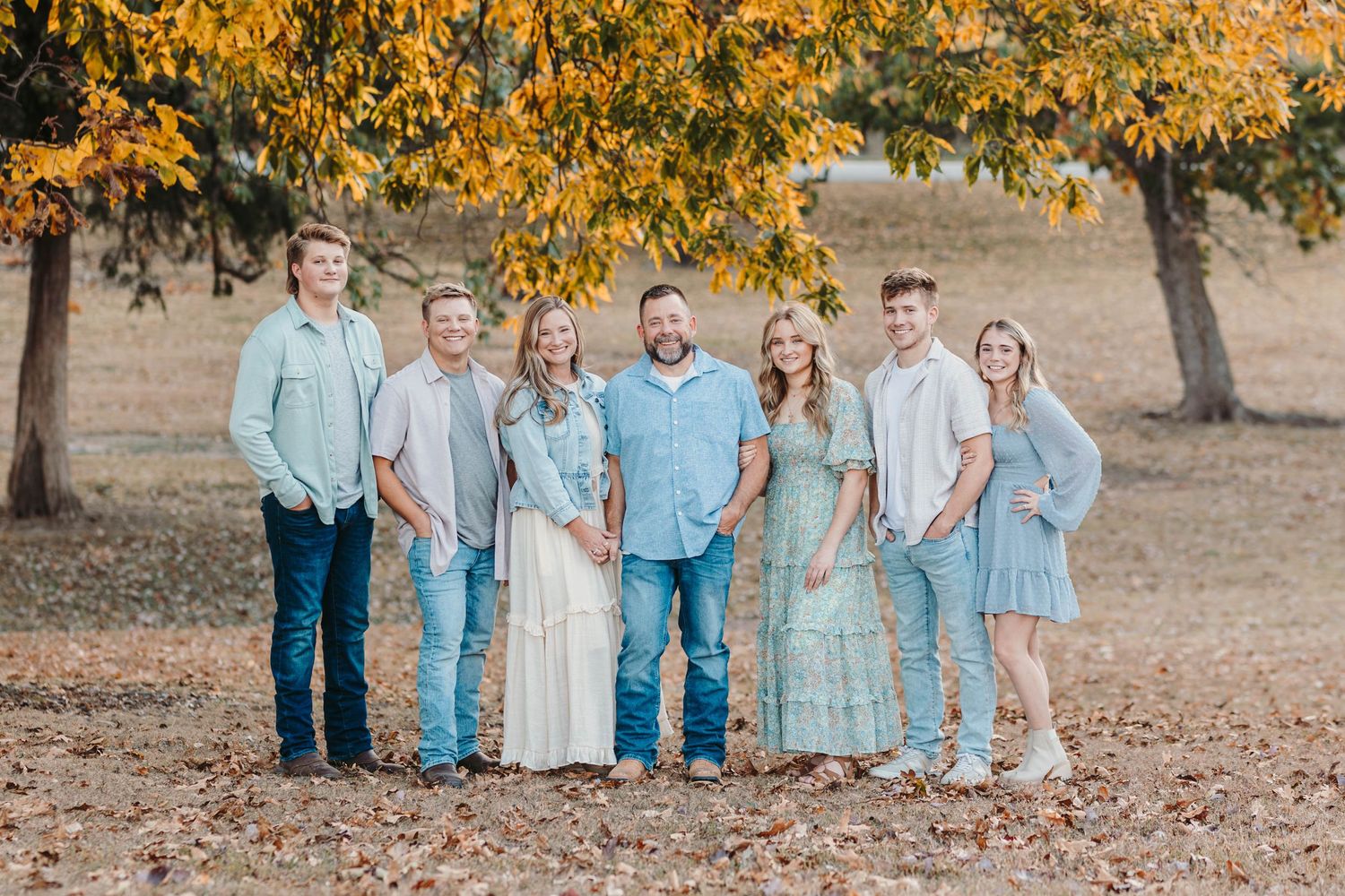Group in coordinated blue and white outfits posed under autumn trees.