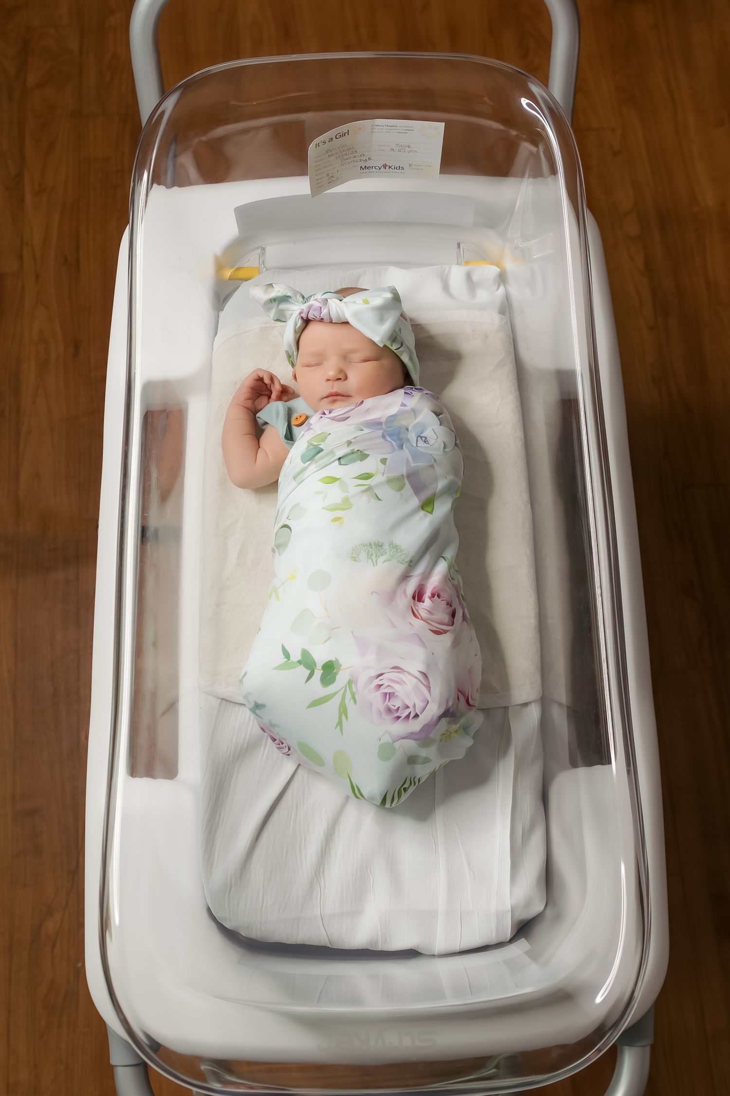 Sleeping newborn wrapped in floral swaddle lying in a hospital bassinet.