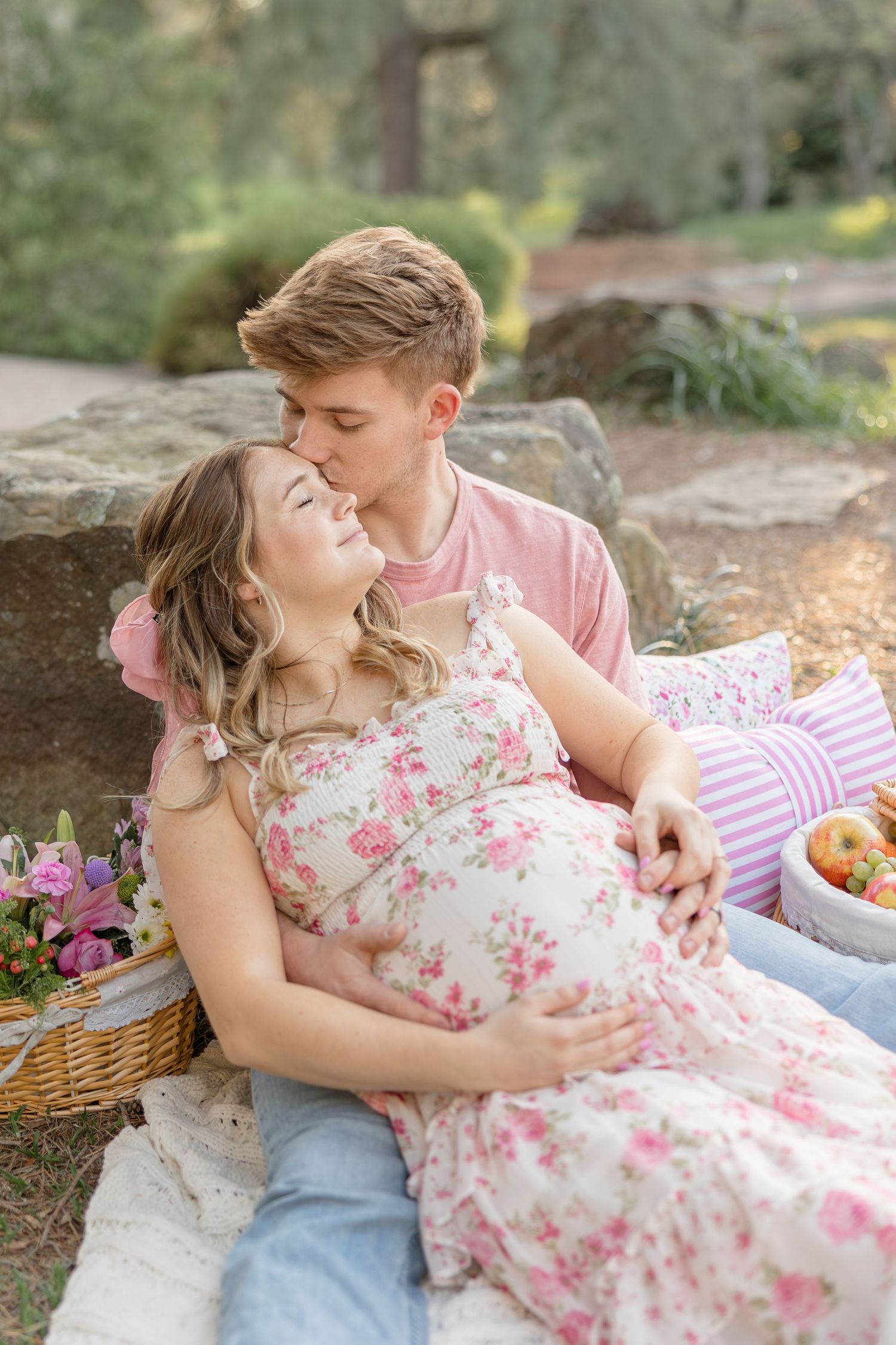 Couple having a romantic outdoor picnic on a blanket with a cozy basket and flowers in a sunlit garden setting.