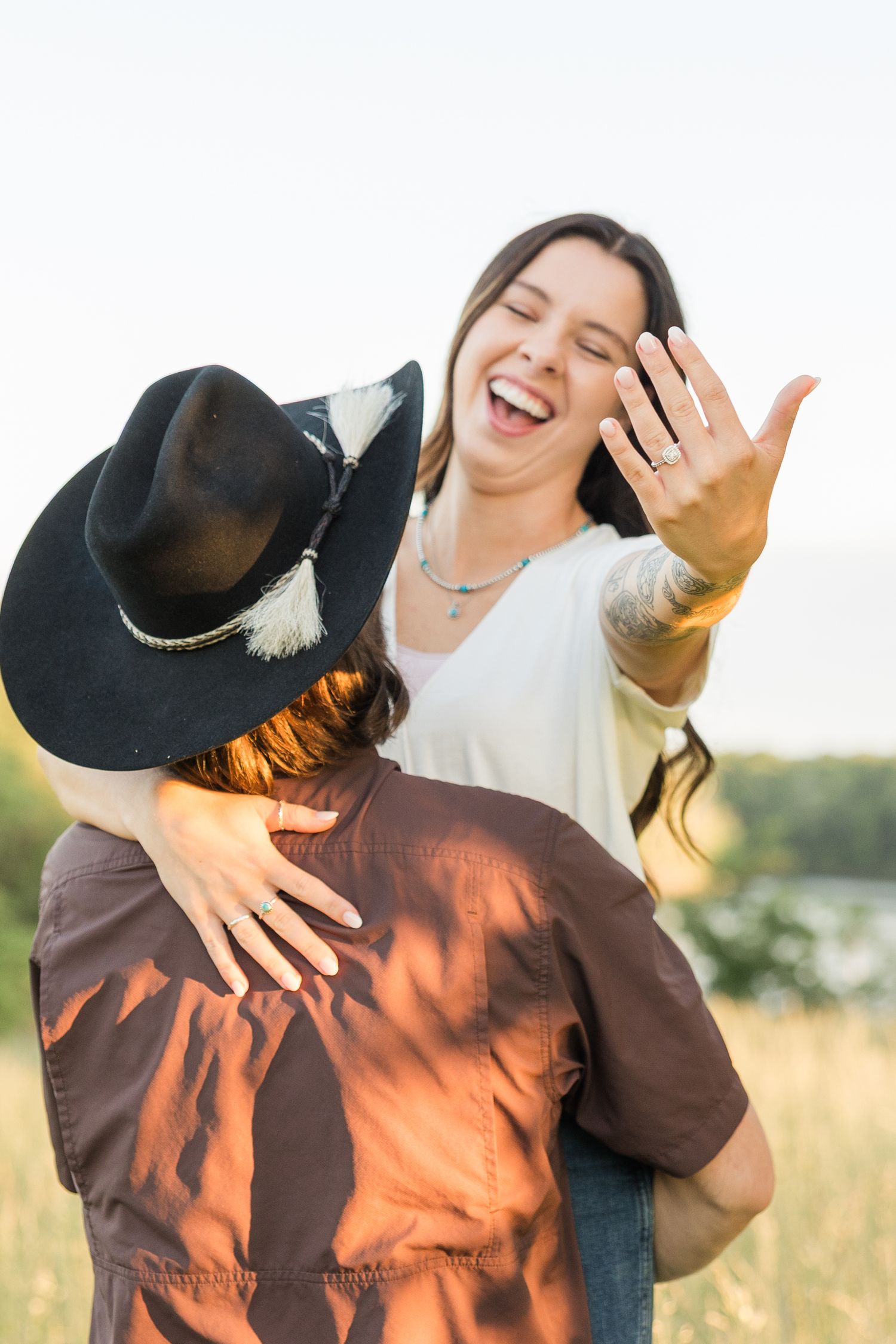 A laughing couple on a field holding hands with one wearing a cowboy hat and western style clothing.