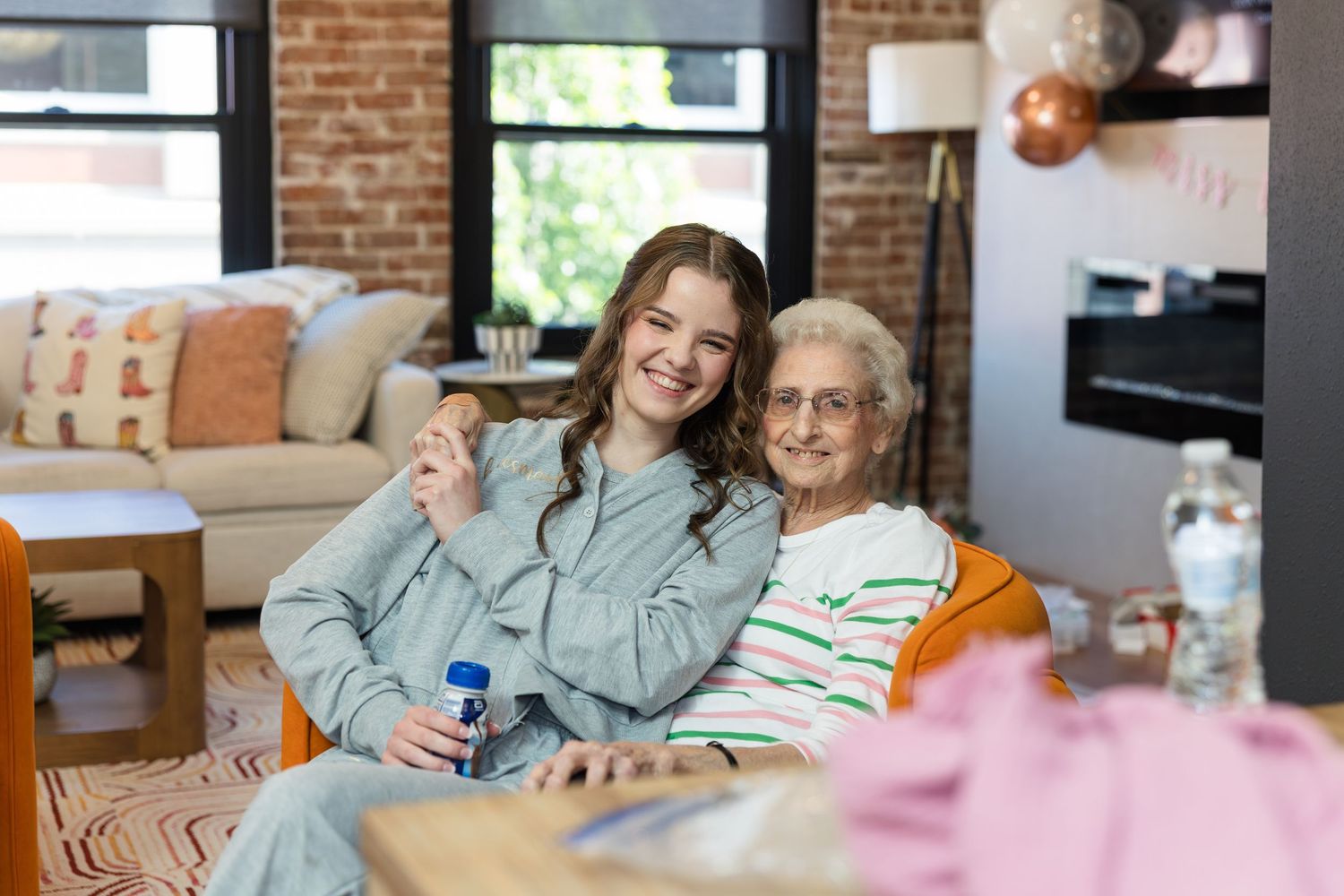 Young woman hugging elderly grandmother on couch in cozy living room, smiling together for a portrait.