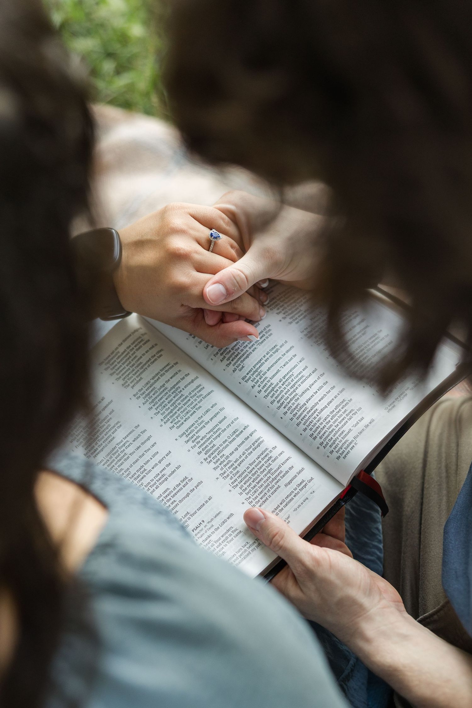 Hands holding open pages of a book in soft natural lighting against a dark background.