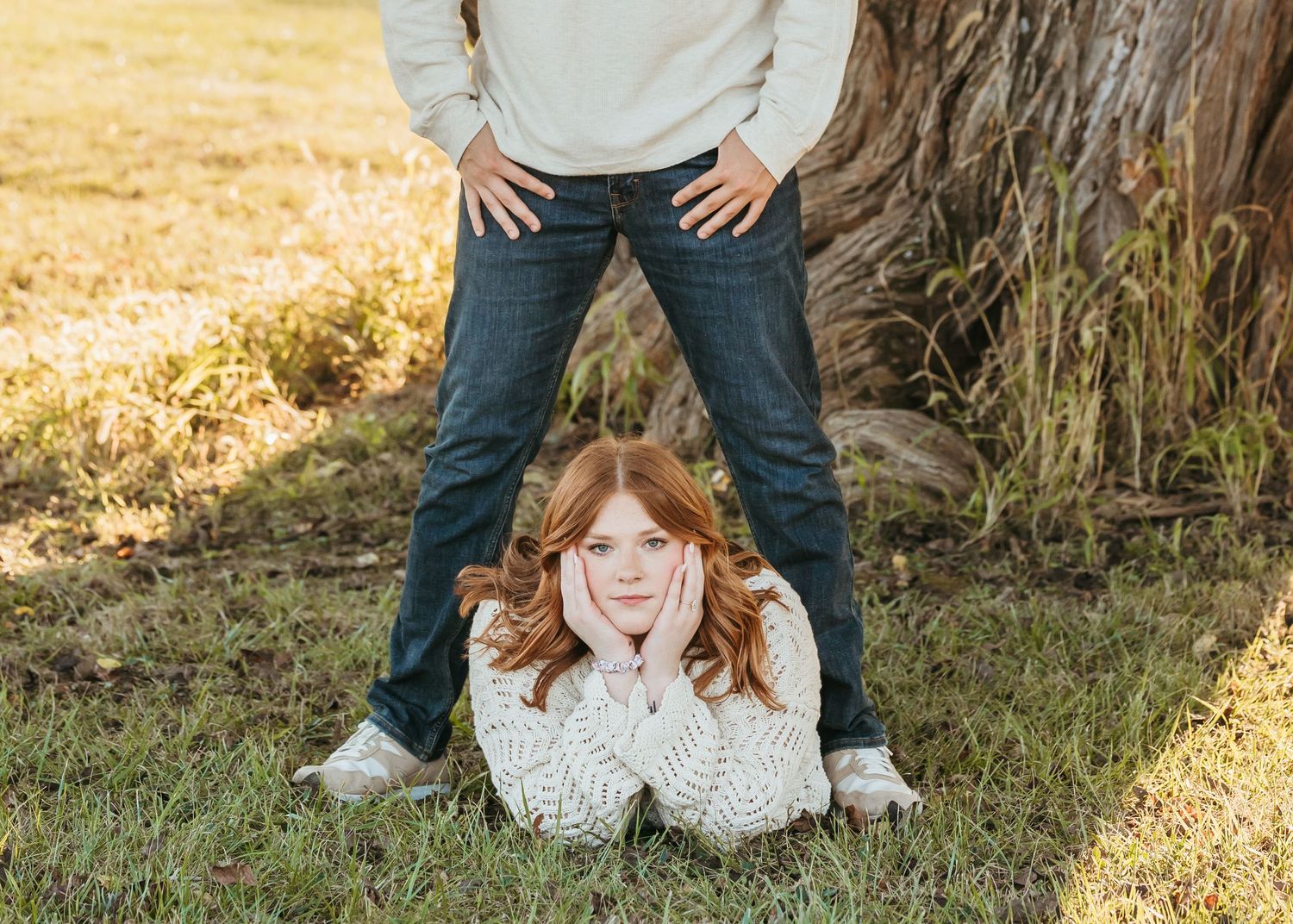Two people pose creatively near a tree trunk in a fun autumn portrait session.
