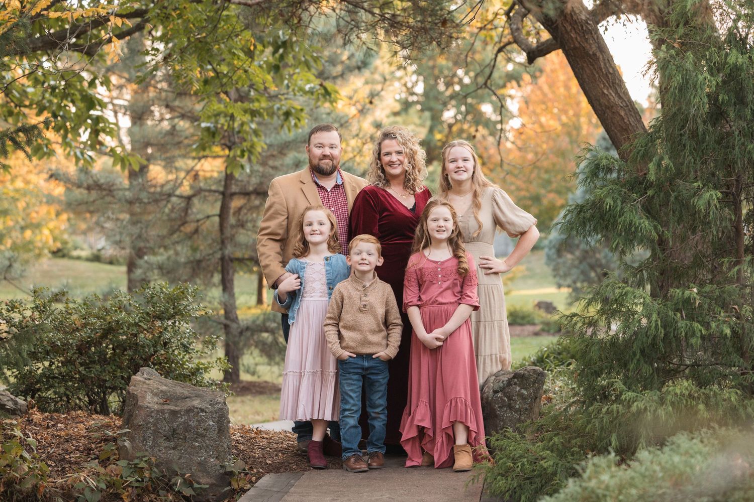 A family group poses together on a path surrounded by autumn trees.