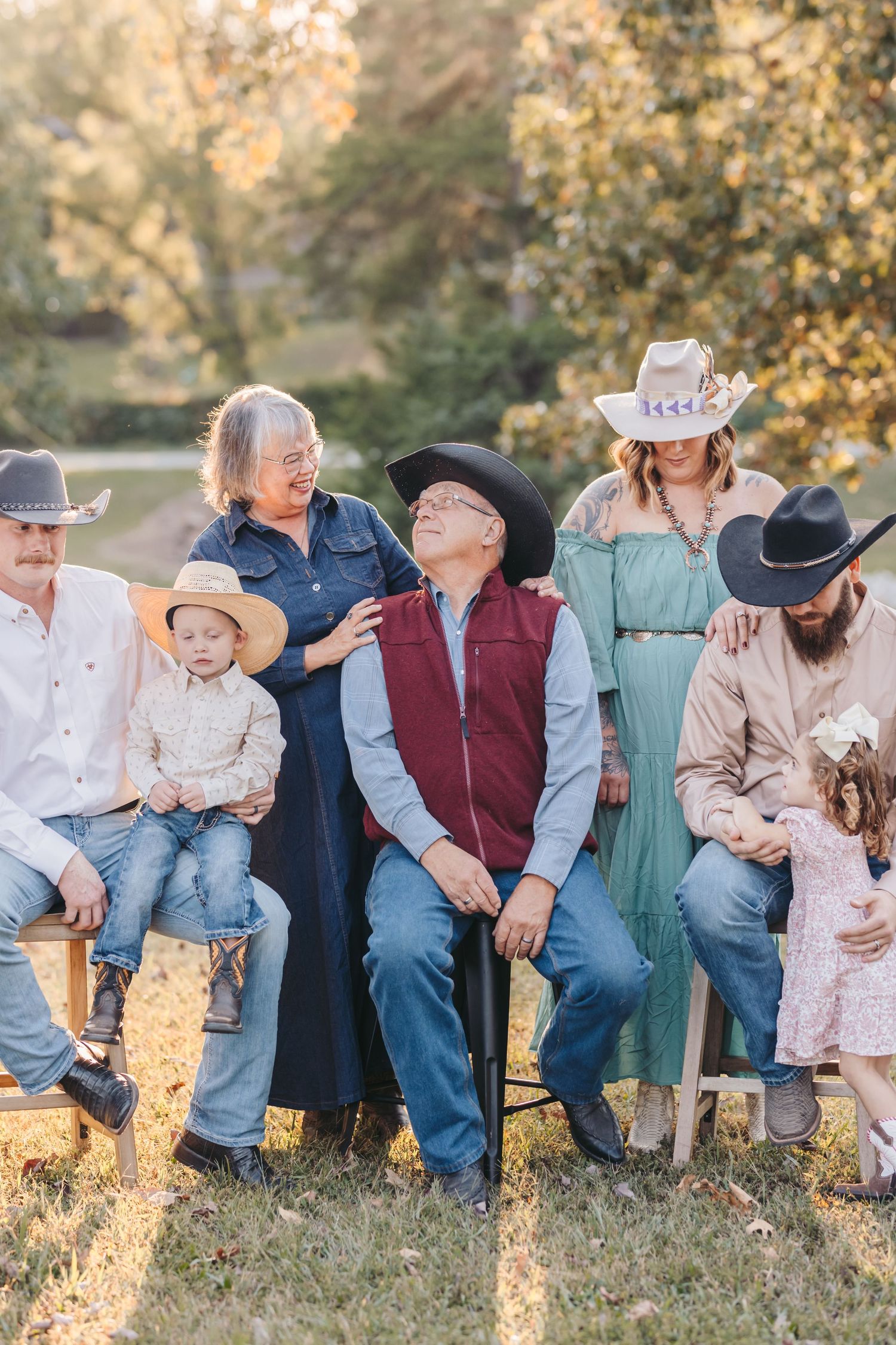 Multi-generational family wearing western clothing sits together on chairs in a sunlit outdoor setting.