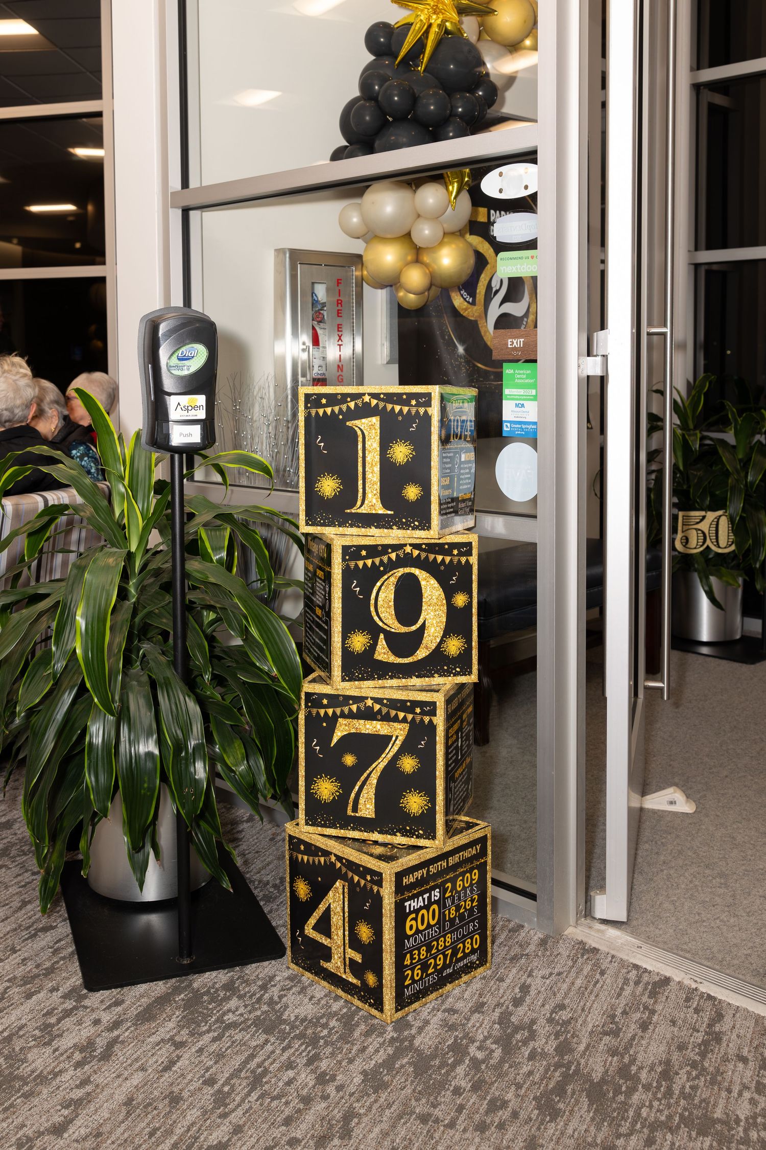Decorative black and gold numbered blocks stacked with balloon arrangements near office entrance.