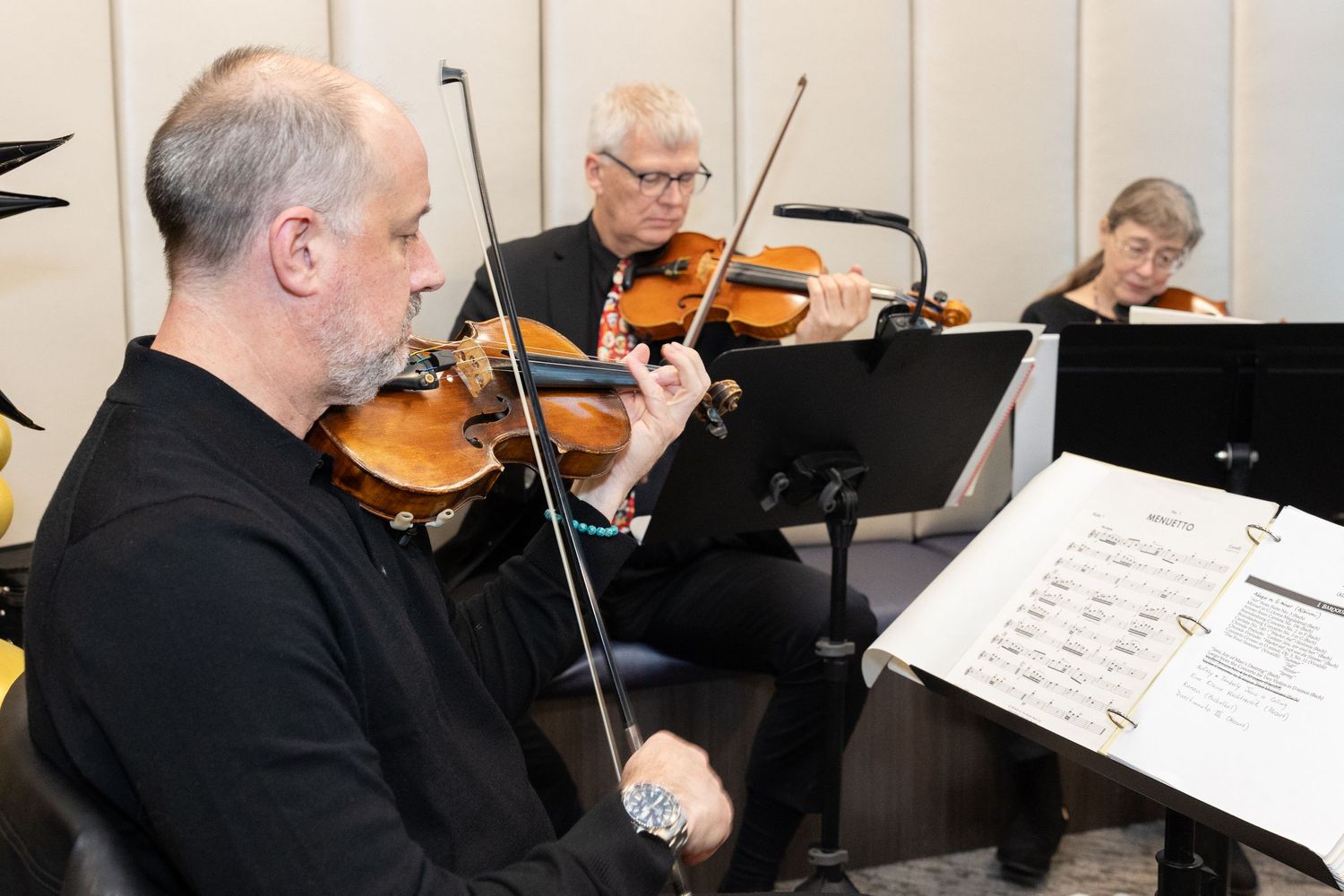 Musicians playing violins while reading sheet music during performance.
