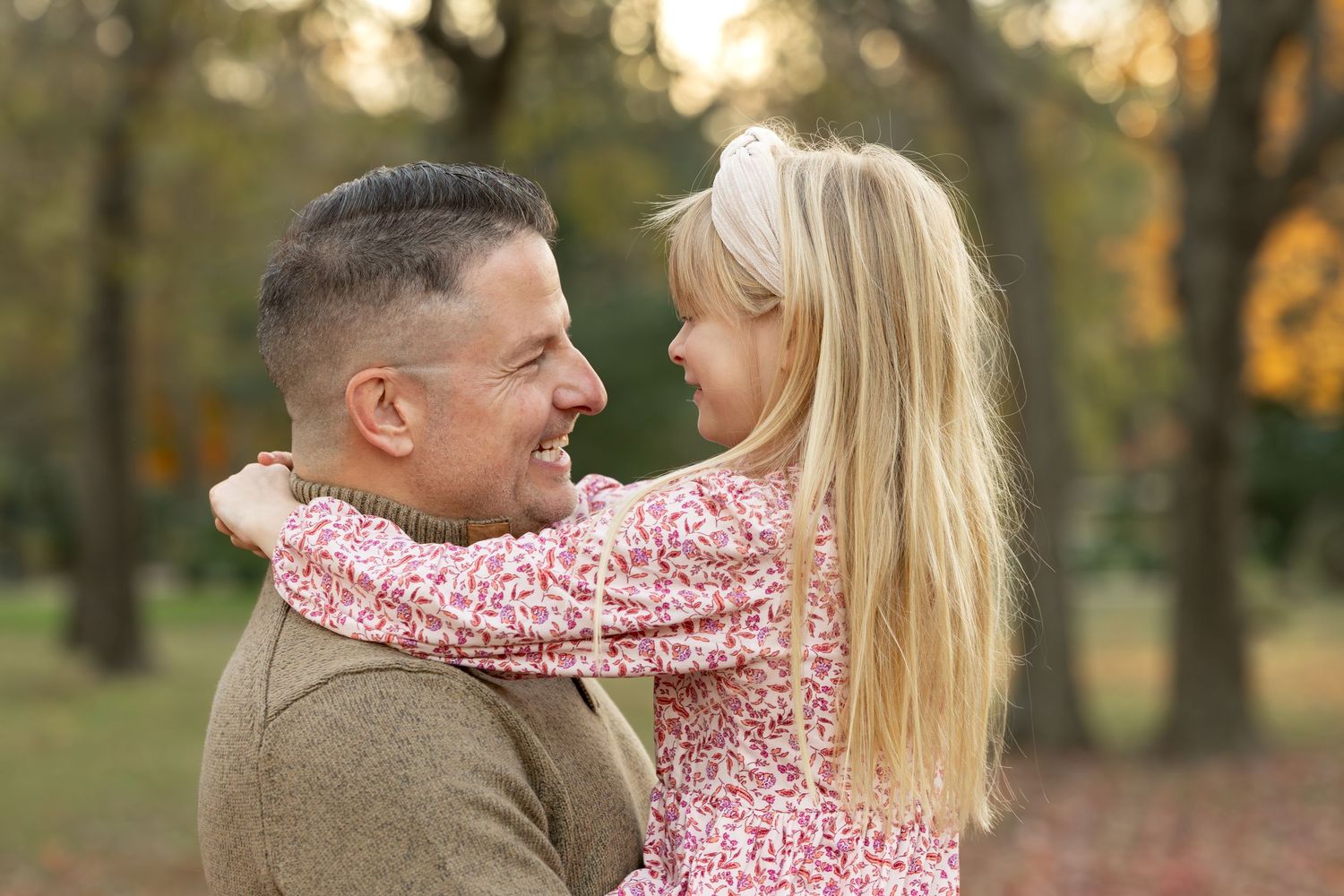A couple embraces in a sunlit park during golden hour wearing pink and white outfits.