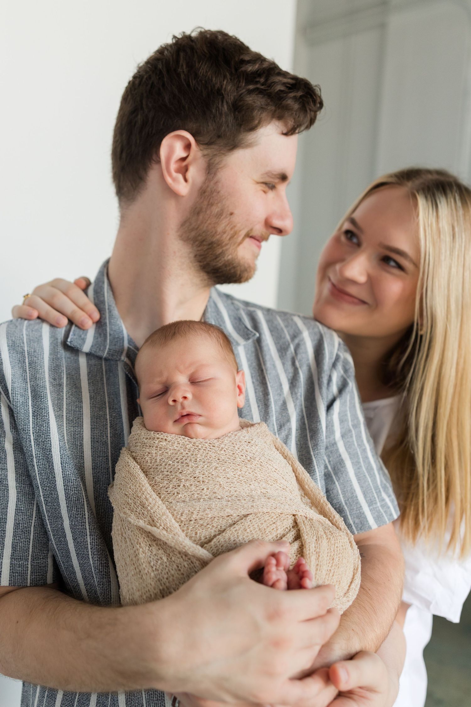 A family shares tender moments together while holding a newborn wrapped in a beige knit blanket.