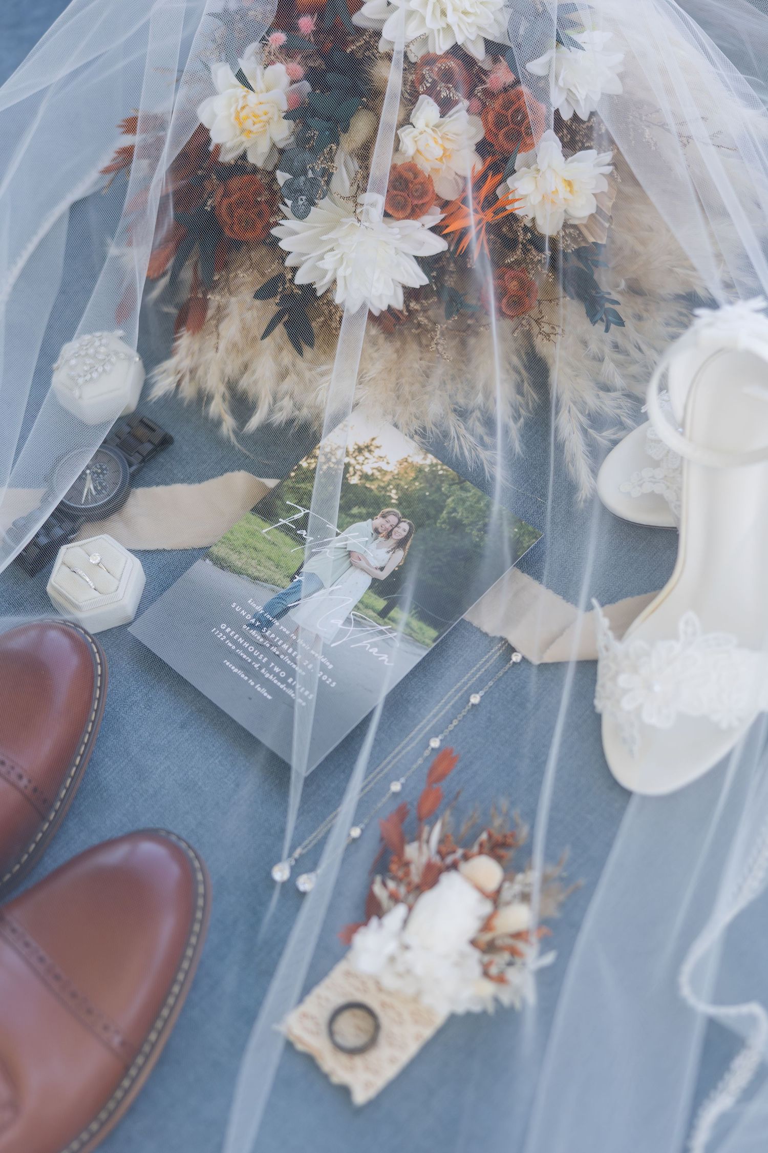 Wedding rings and delicate white flowers rest on a soft blue tulle veil with romantic styling.