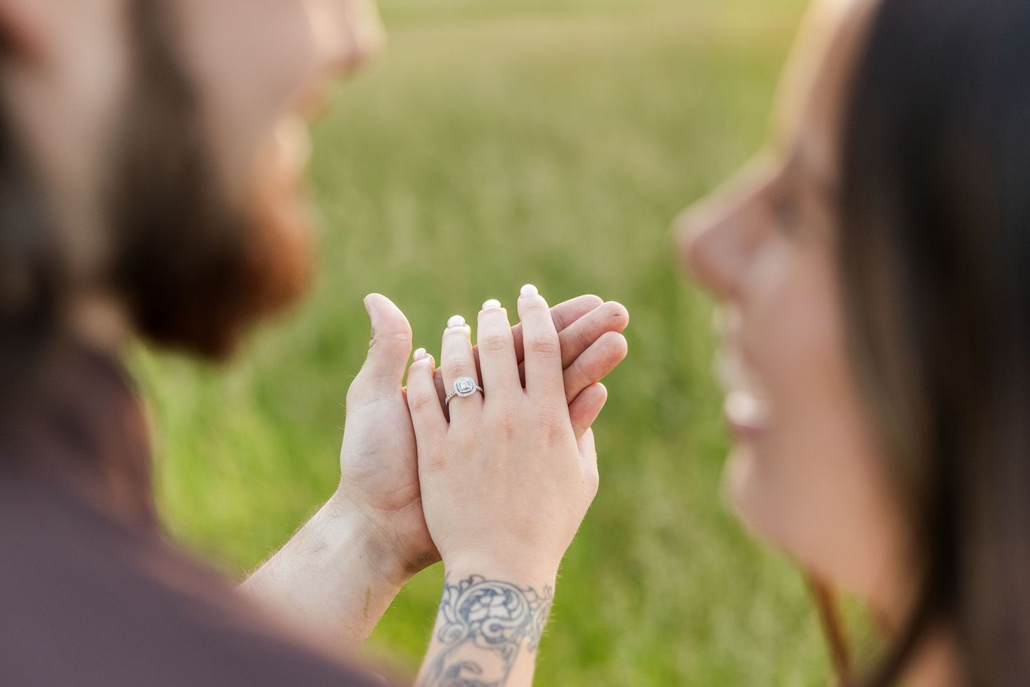 Two people hold hands tenderly in an outdoor setting with visible tattoos and sunlight filtering through.
