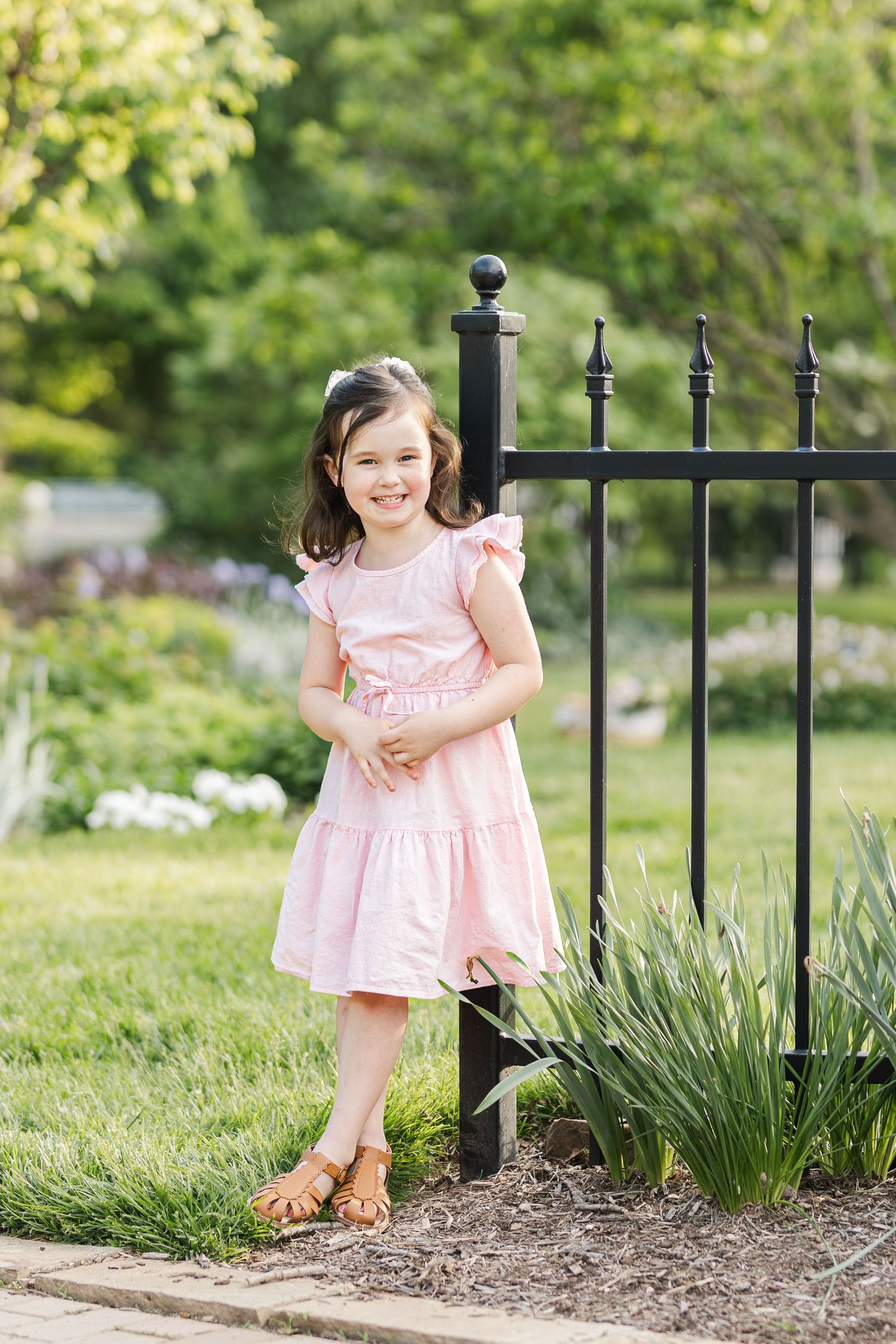 A pink dress stands out against a wrought iron garden fence and lush greenery in a springtime setting.