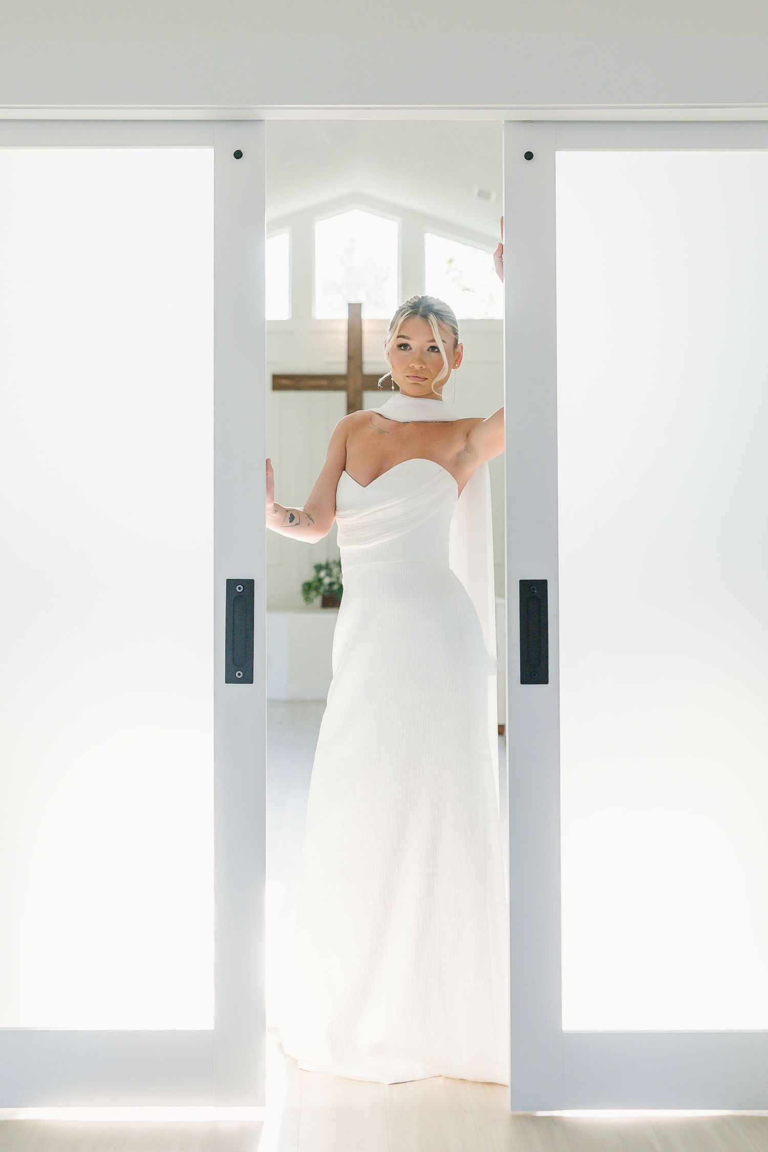 Color portrait of a bride wearing a flowing strapless white wedding dress posing in a bright doorframe.