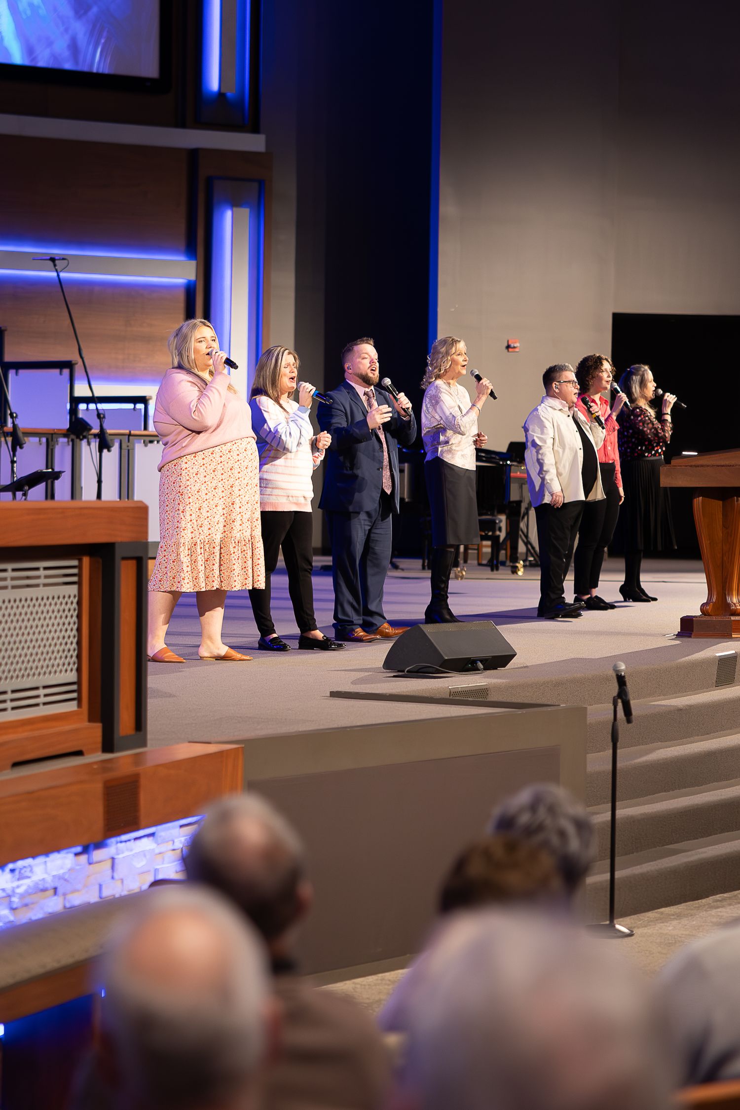 Musicians and singers performing on modern church stage with blue lighting effects.