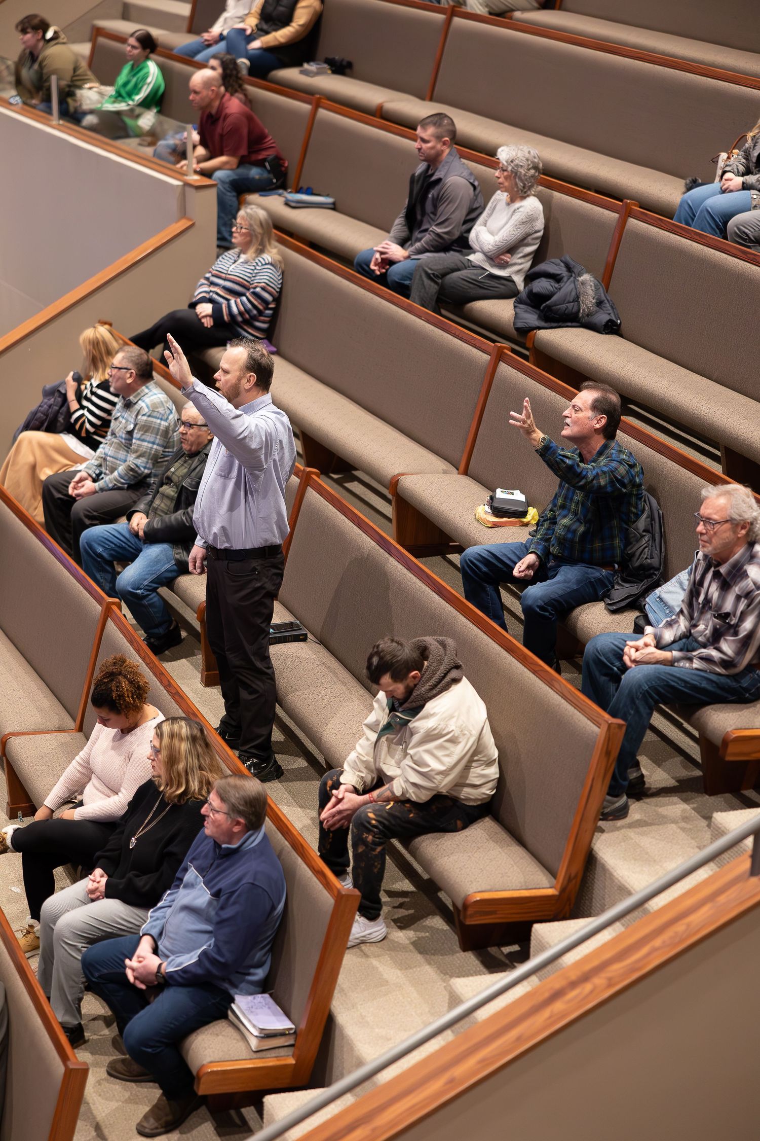 Church congregation seated in tiered wooden pews during worship service.