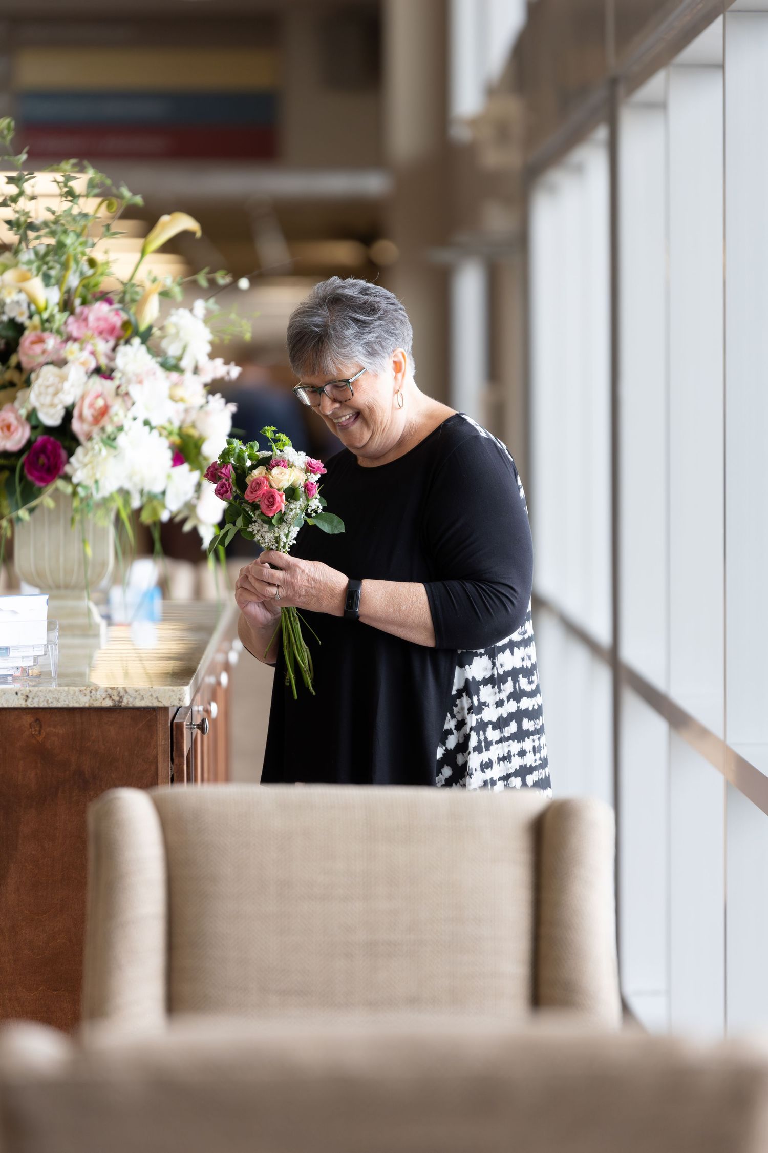 A person arranging colorful flowers in a vase near a bright window.