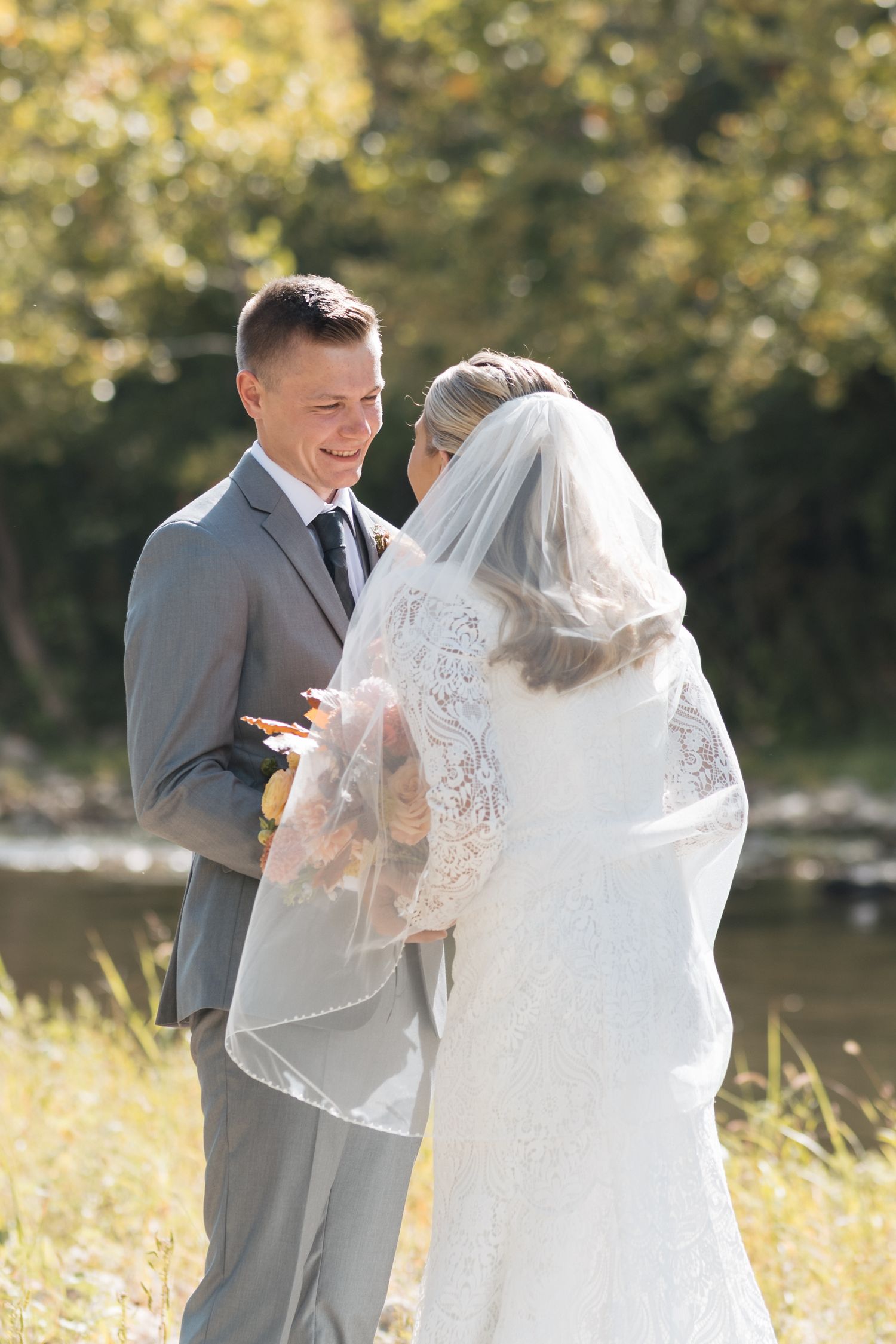 A newlywed couple shares an intimate moment during their outdoor wedding ceremony by a lake.