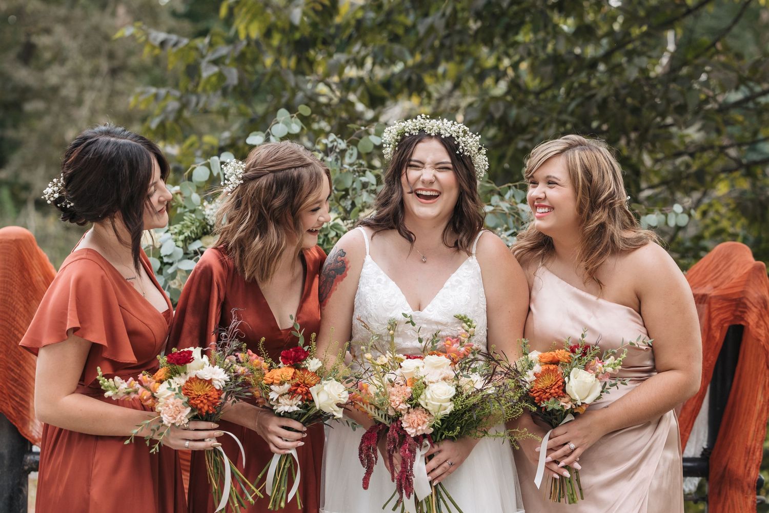 Wedding party in warm autumn tones holding bouquets and sharing joyful moment.
