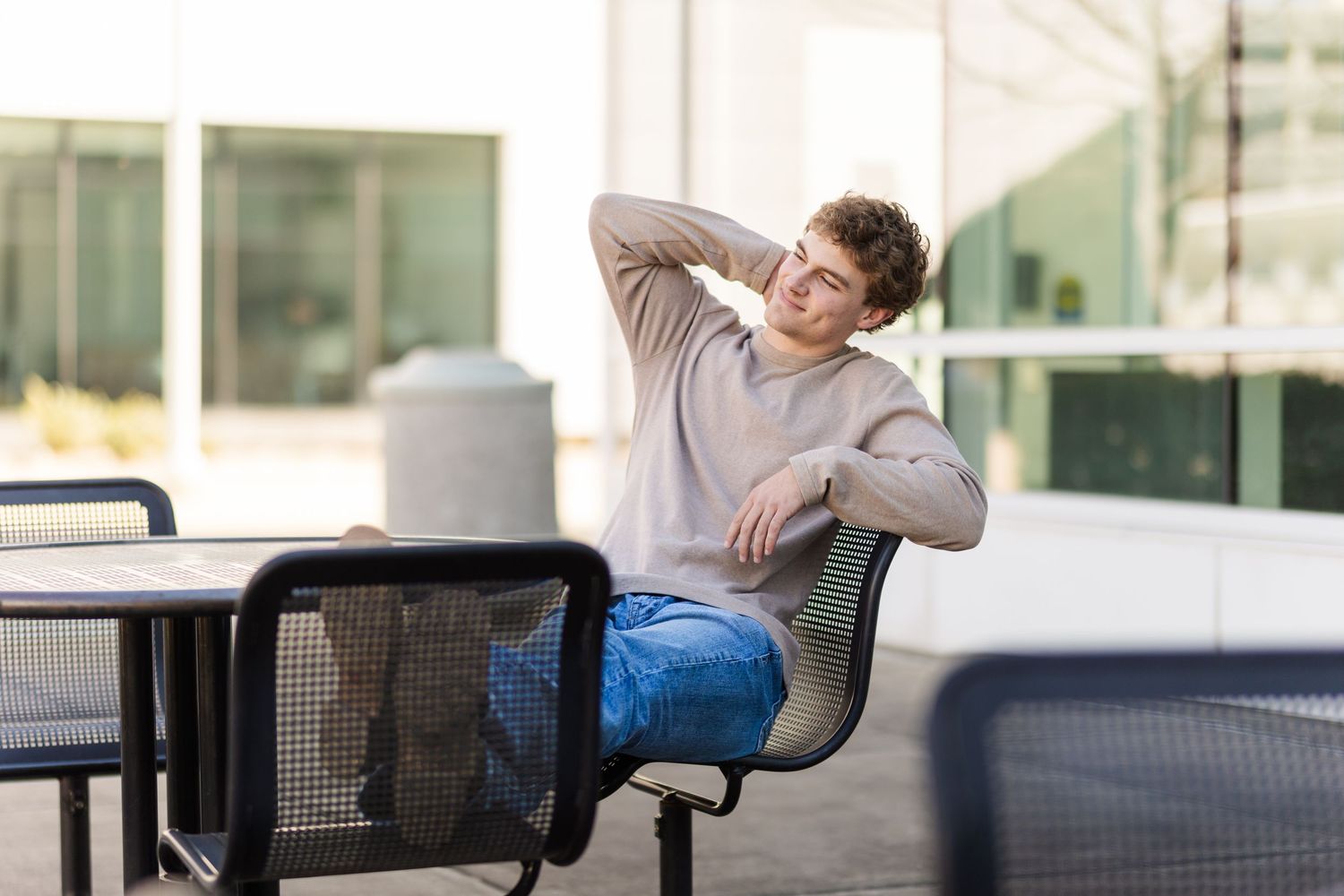 Student relaxing in casual attire while sitting outdoors at a table on campus.