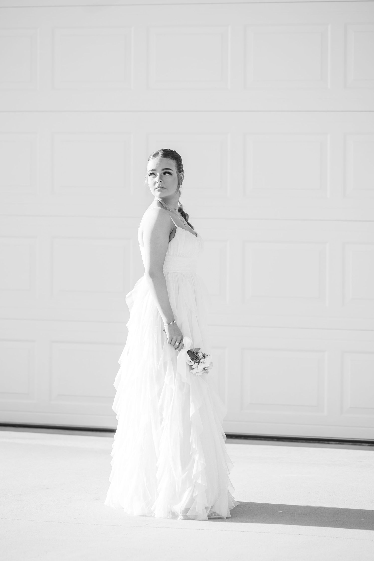 Elegant black and white bridal portrait featuring a strapless white gown against a minimalist white garage door background.
