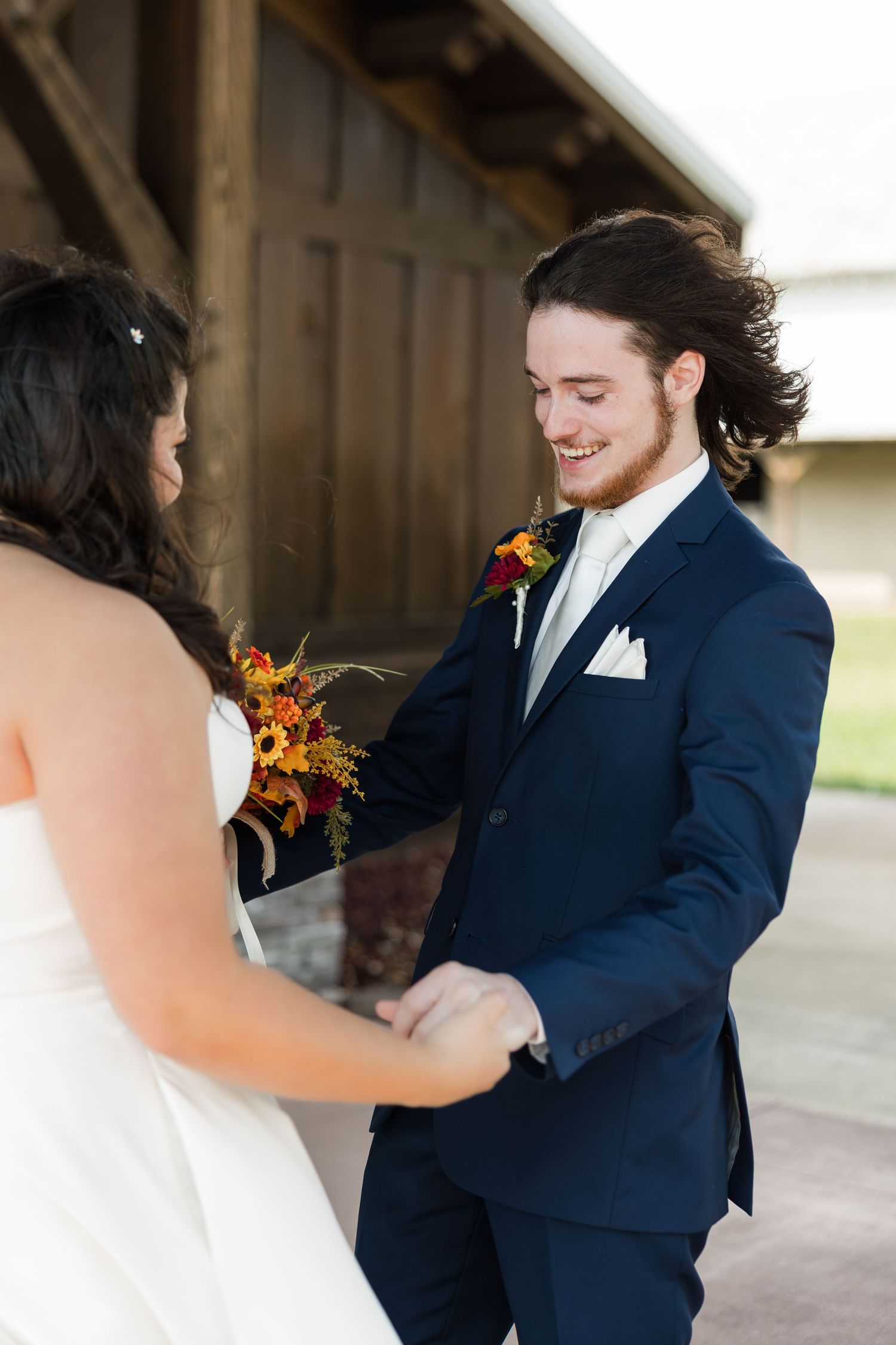 A romantic first look moment between a couple, with the groom in navy suit and bride holding autumn flowers.