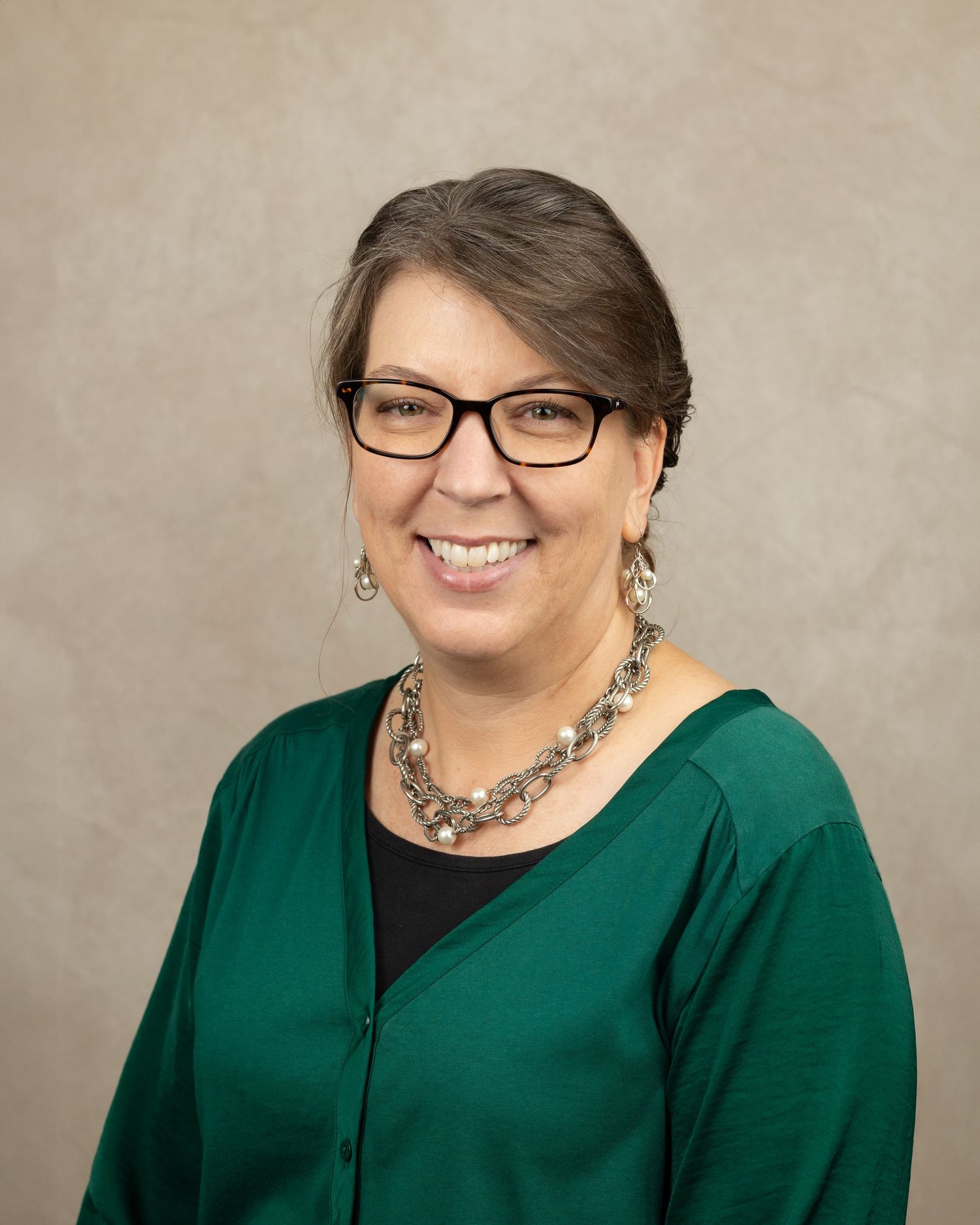 Professional headshot of woman in green top wearing glasses and statement necklace.