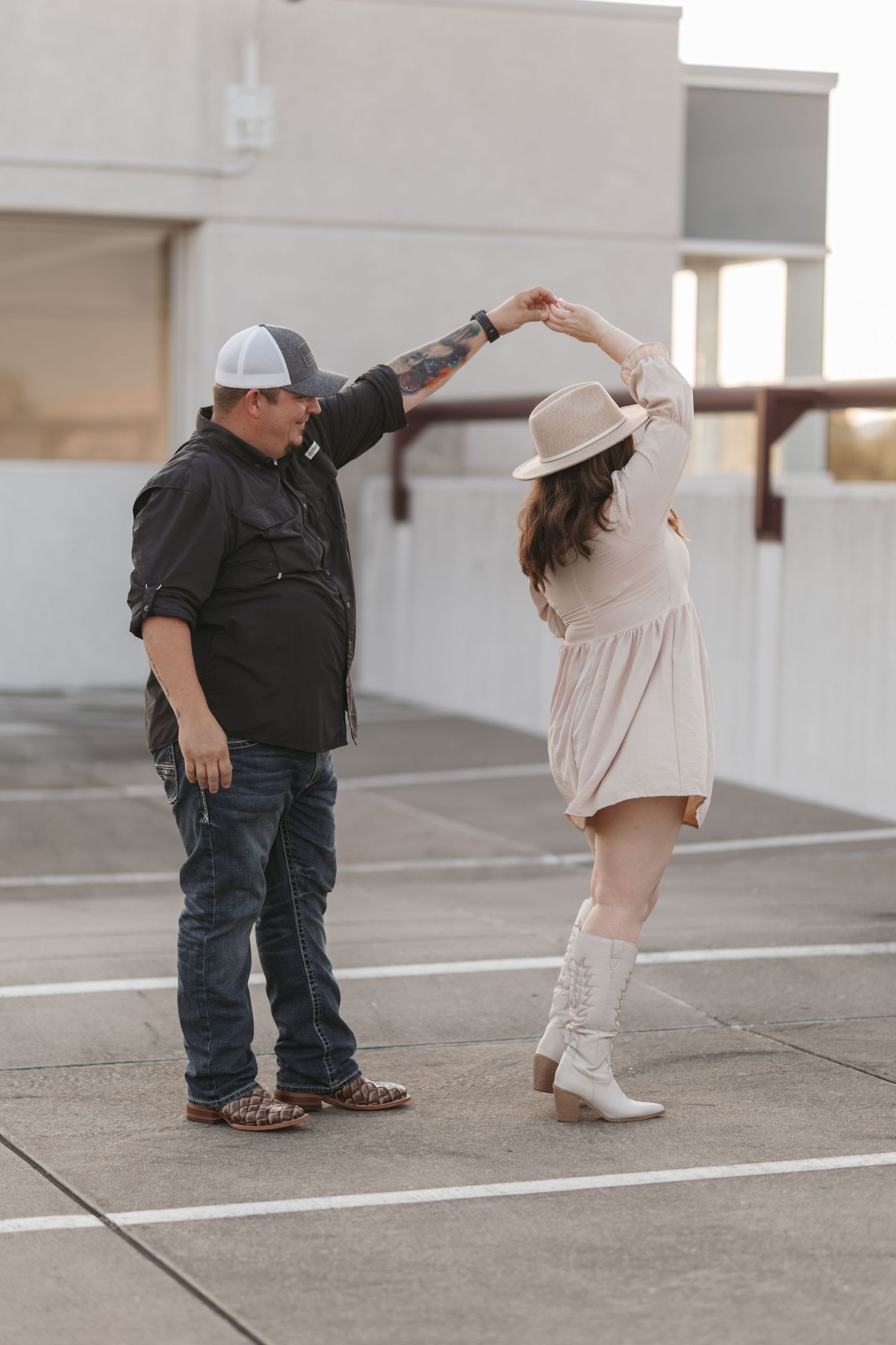 Couple dancing in parking structure, twirling in western-inspired outfits.