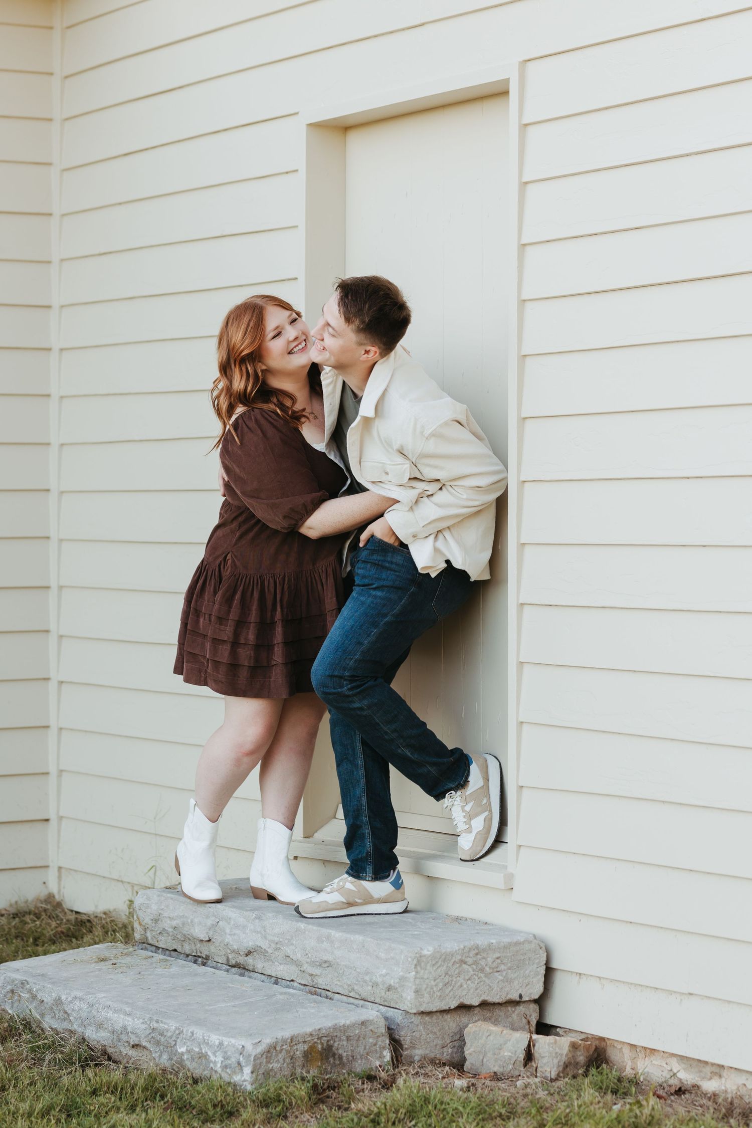 Couple in casual attire sharing an intimate moment against a white wall with the woman wearing white boots.